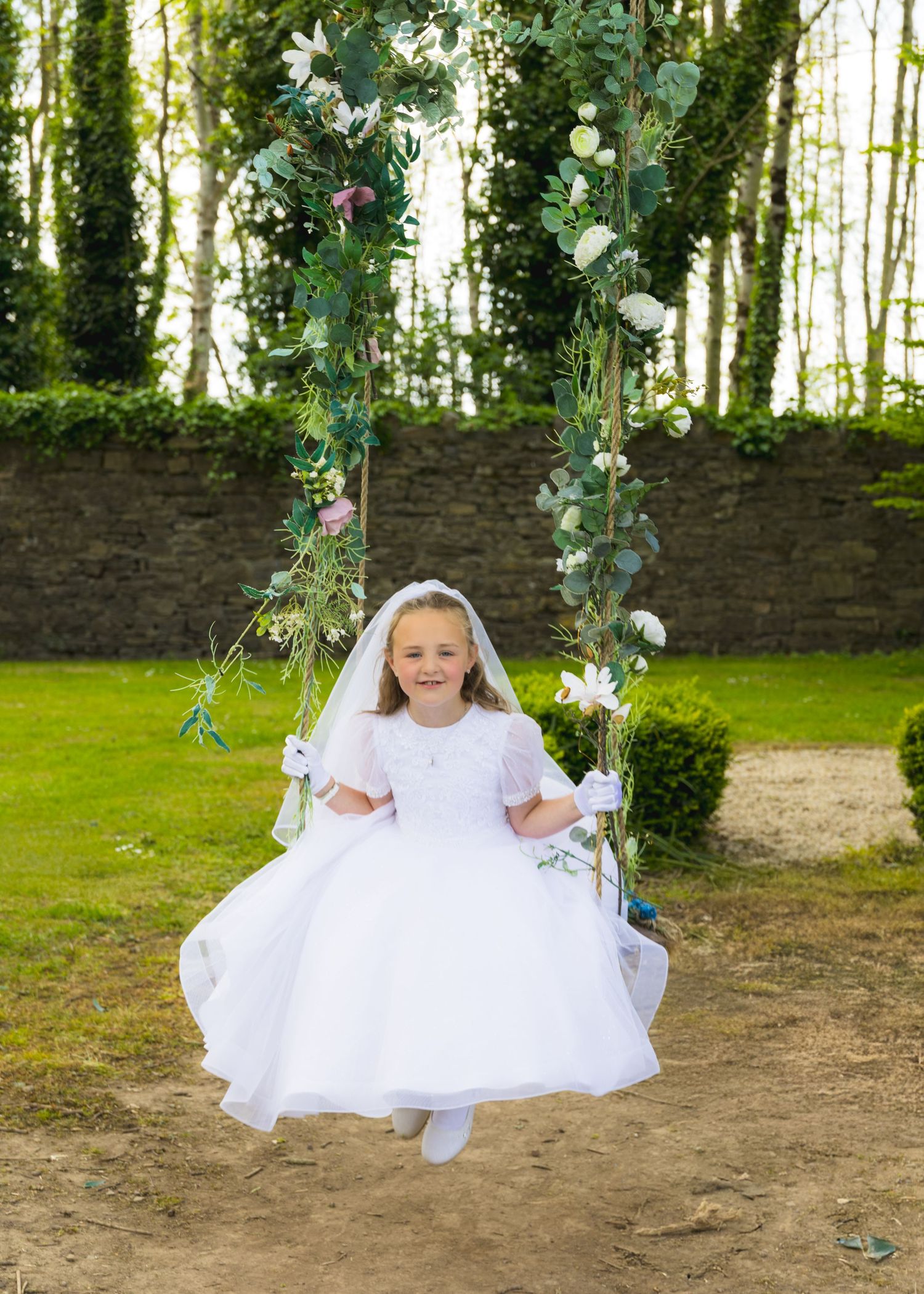 A child in white dress sitting on a decorated garden swing.