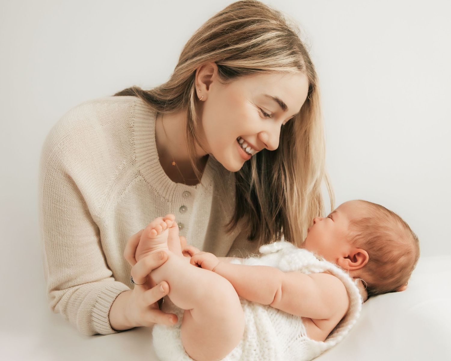 Smiling young mother holding her newborn baby, sharing a tender moment against a white background.