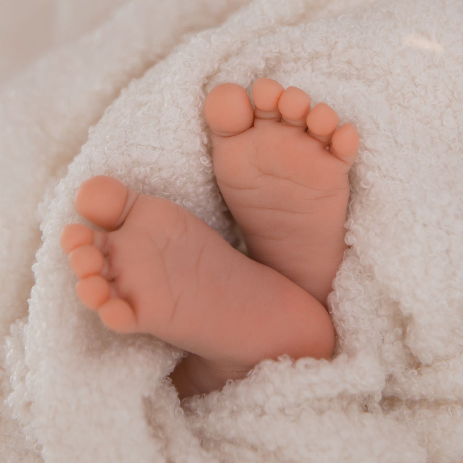 Close-up of tiny newborn baby feet peeking out from a soft white fluffy blanket.