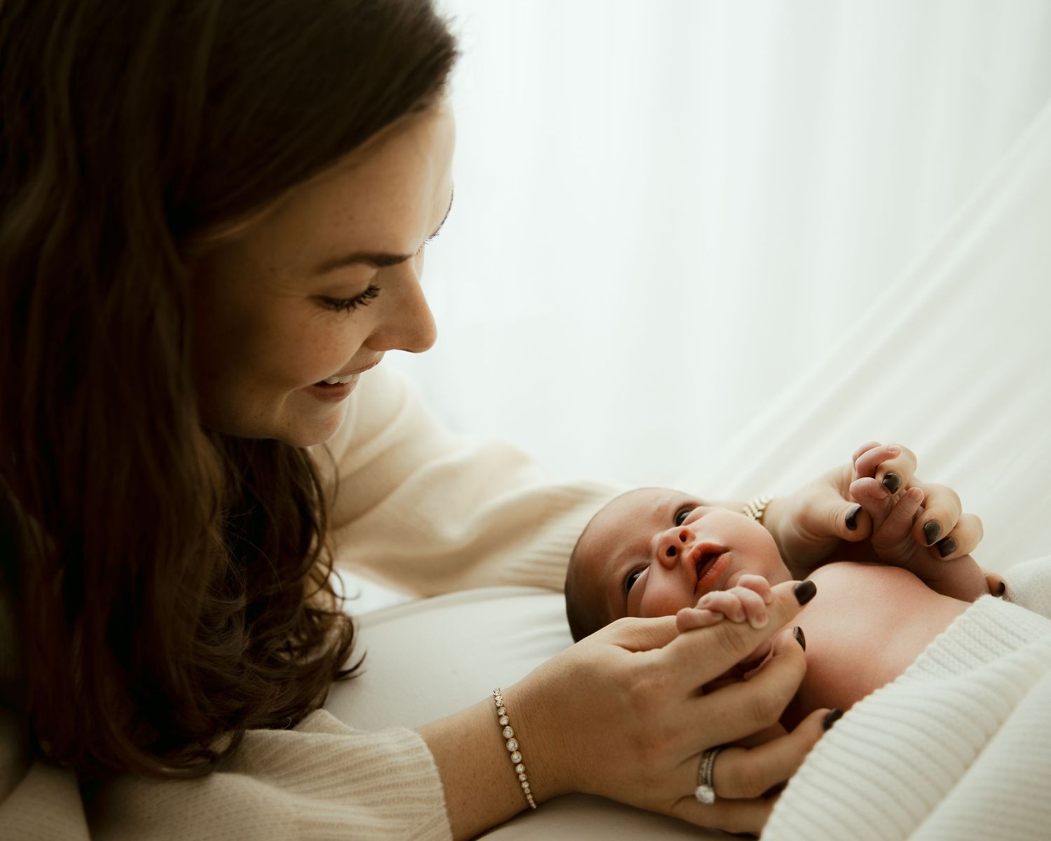 Gentle close-up shots of mother bonding with newborn on white bedding.