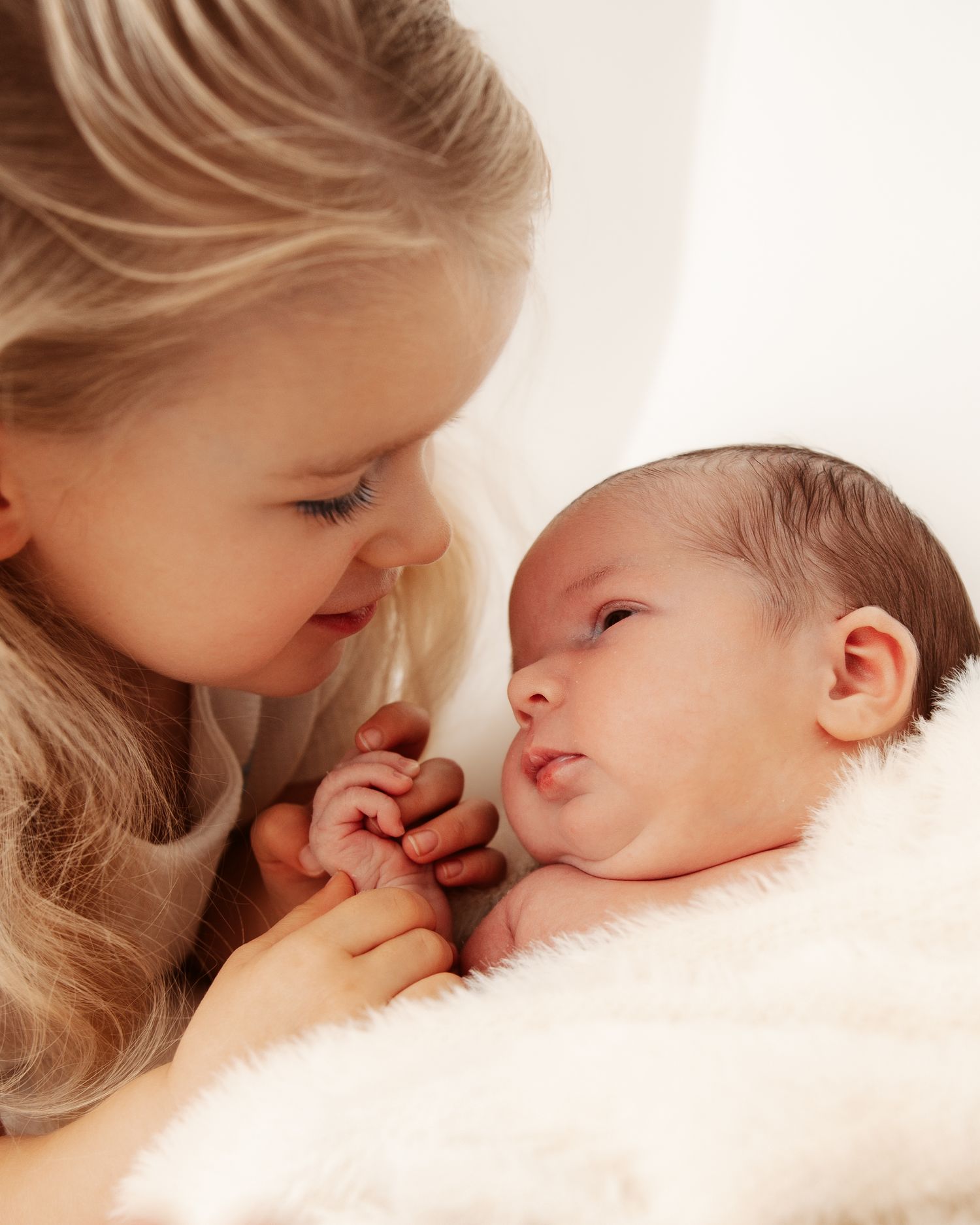Sweet close-up sequence of a child gently kissing a sleeping newborn baby on soft white bedding.