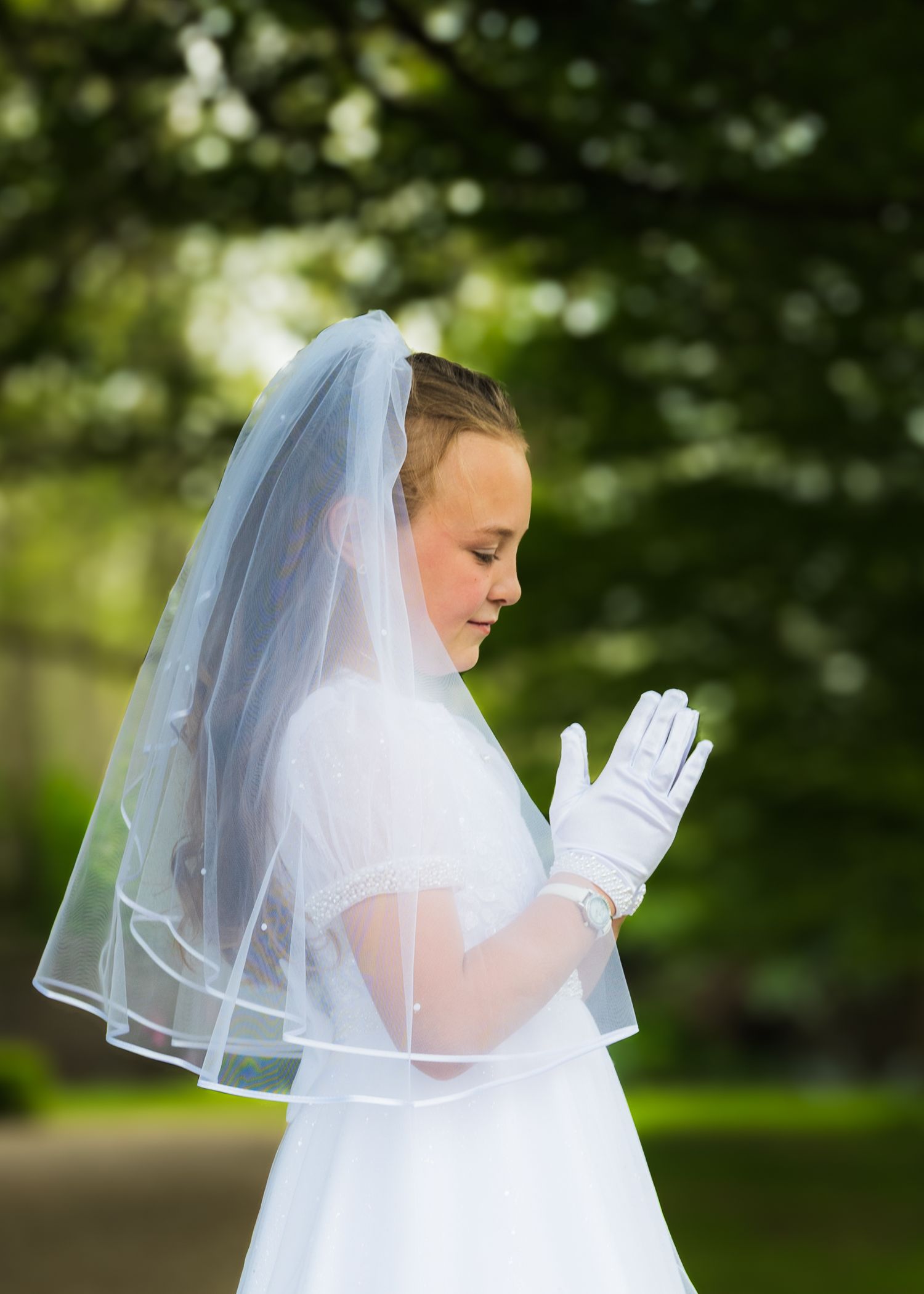A figure in white dress and veil photographed in an outdoor setting.