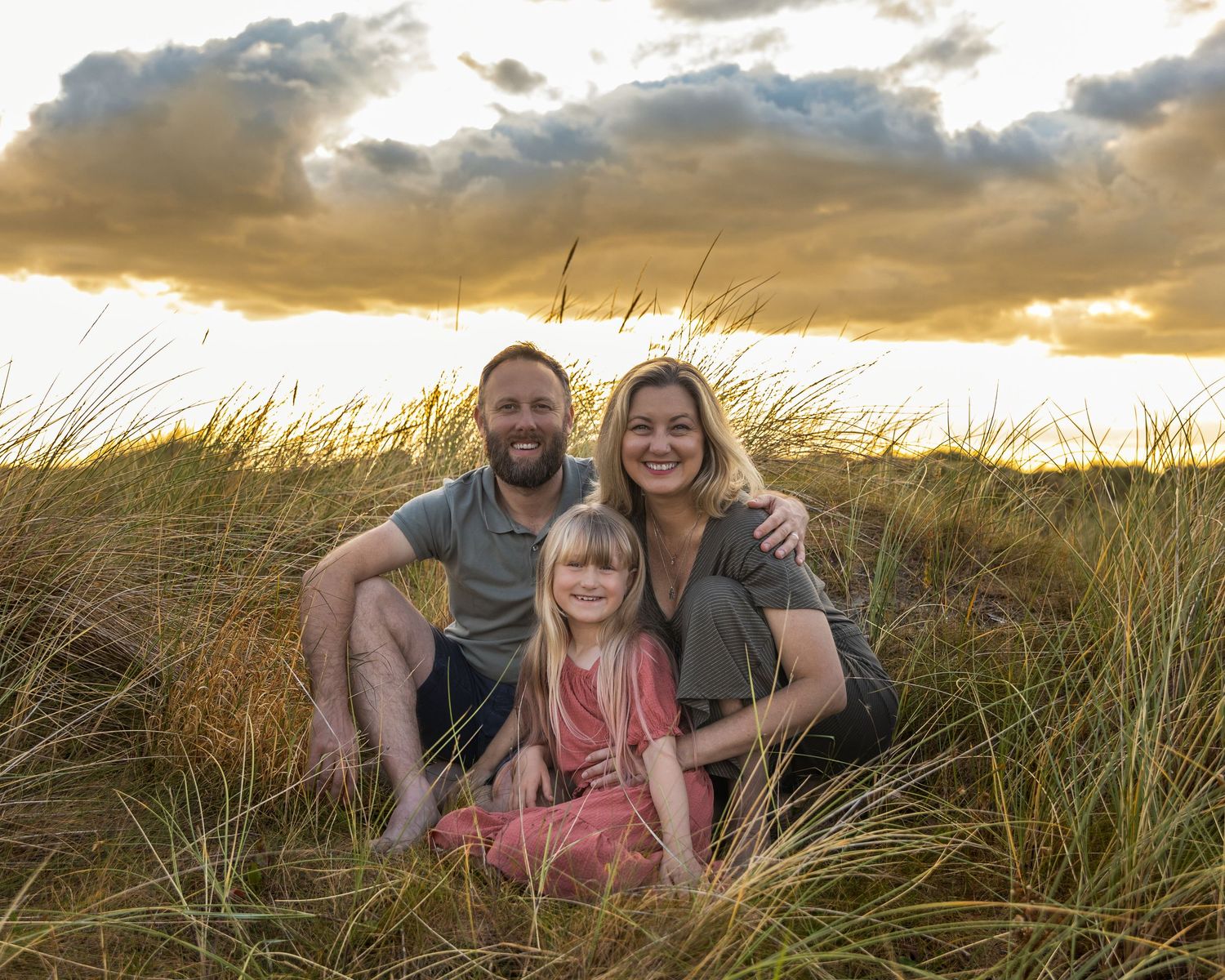 Family relaxing together in coastal dunes during golden hour photography session.