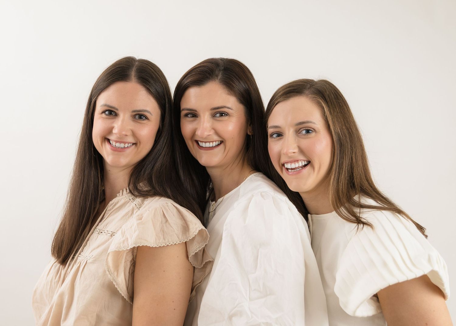 Close-up portrait of people in white tops smiling against white background.