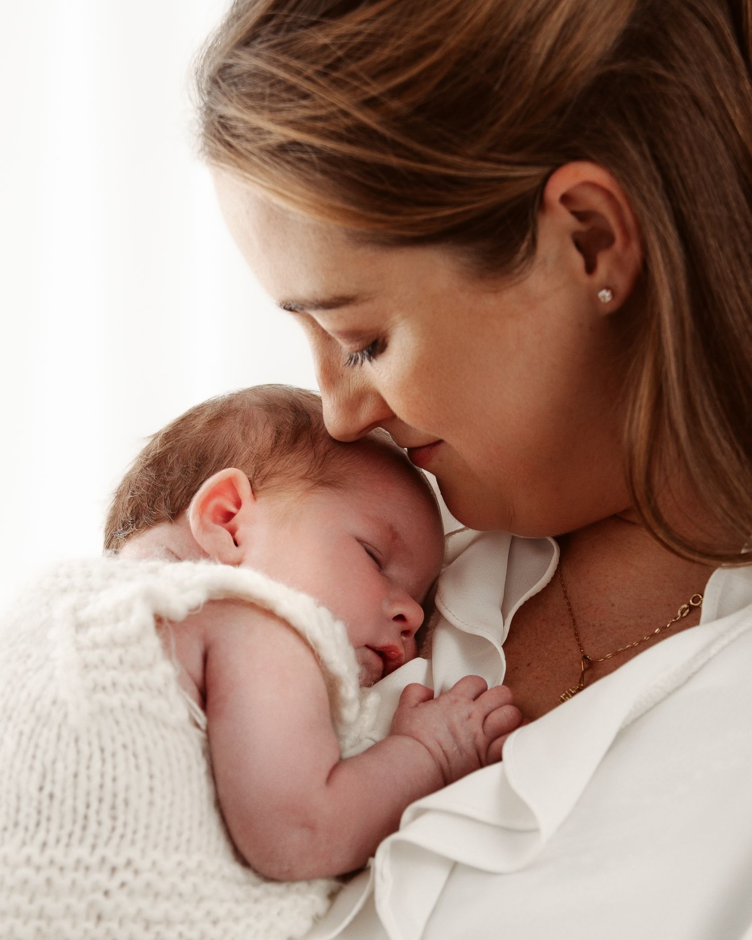 Intimate moments captured between mother and newborn baby in soft white setting.