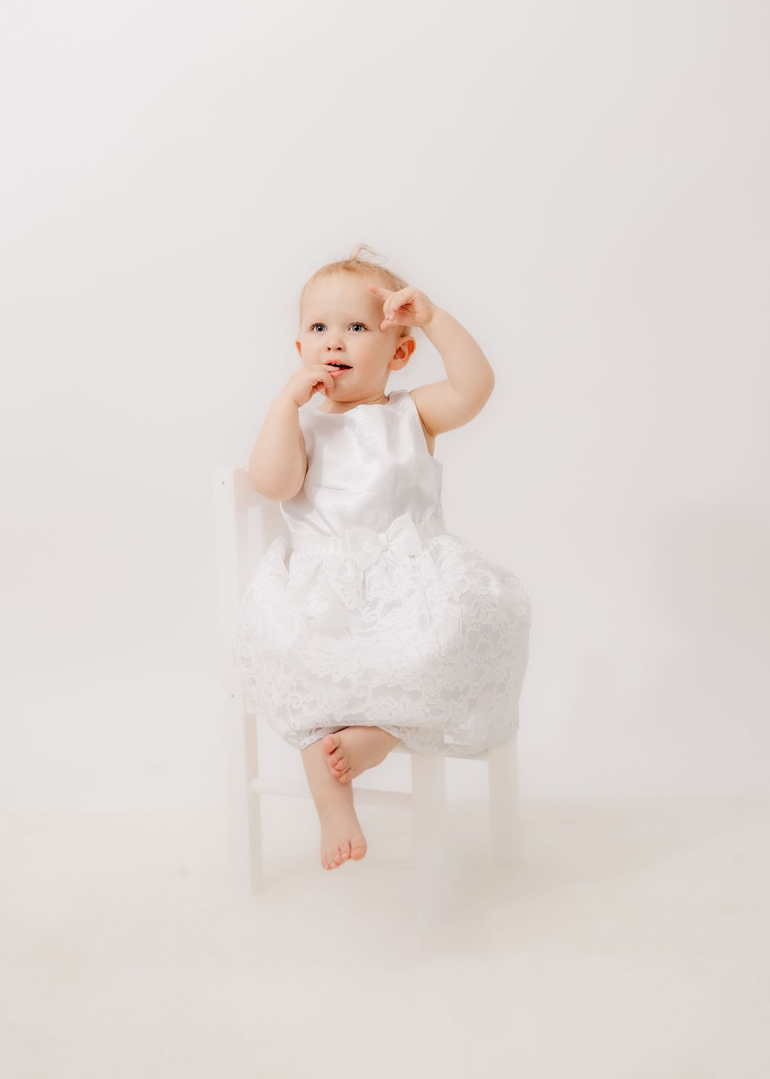 Four images of a baby in white lace dress sitting and playing on a light background in a photography studio.
