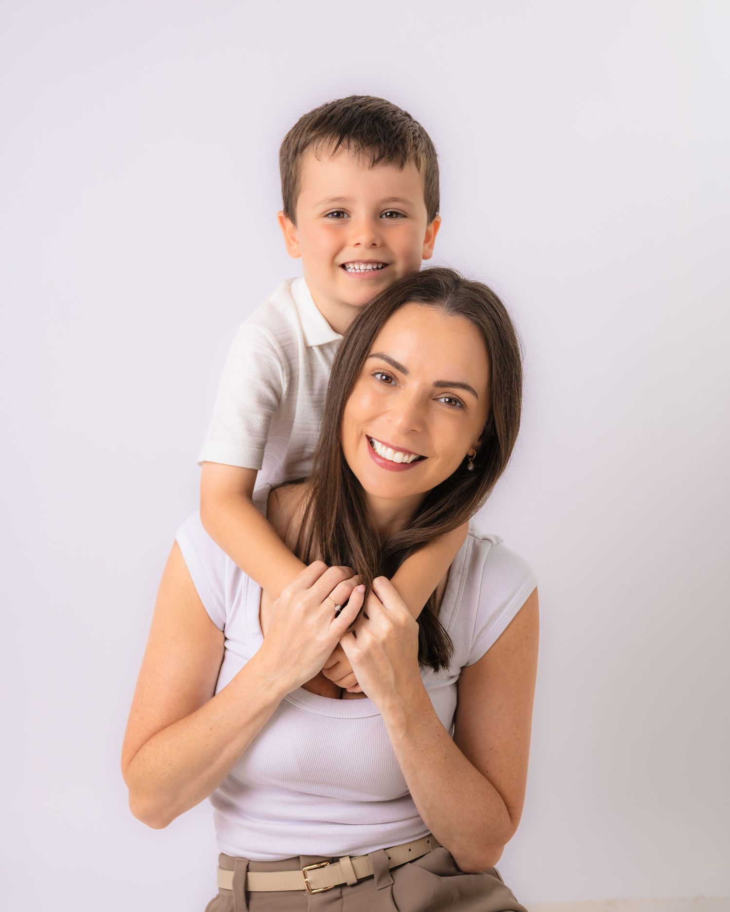 A smiling woman and young boy pose together, with the child sitting on her shoulders against a white background.