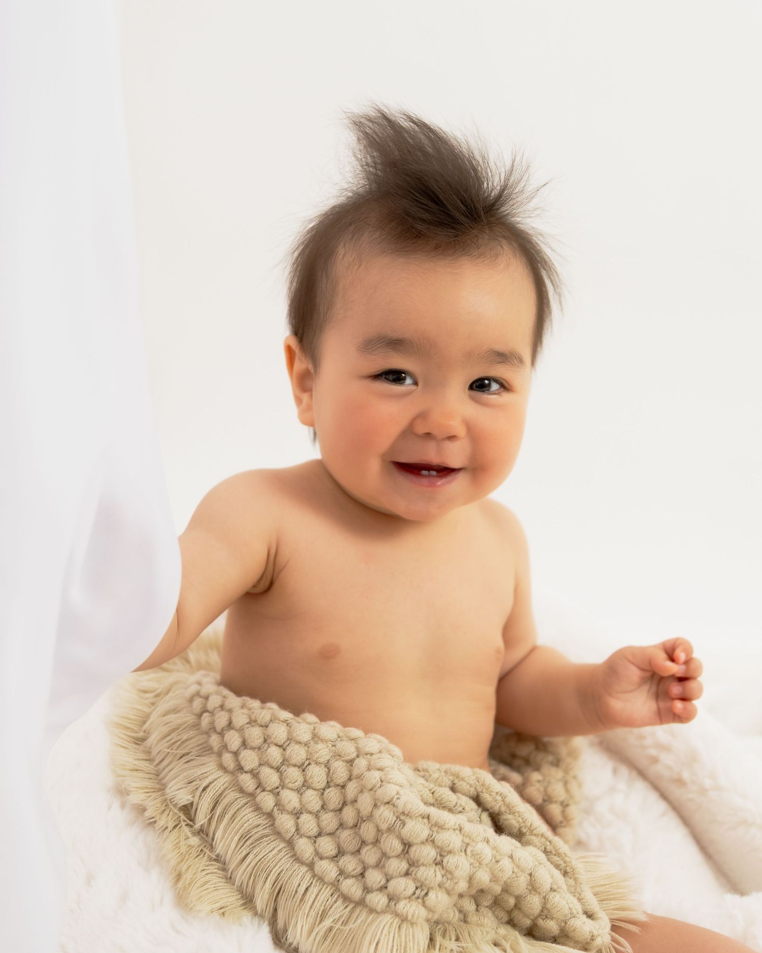 Baby wrapped in cream textured blanket smiling during studio photoshoot.