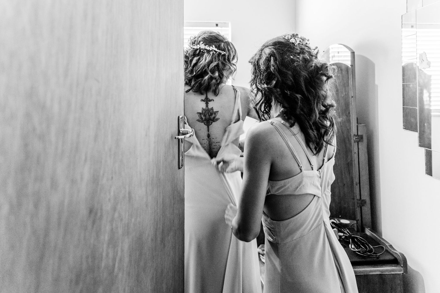 Black and white photo of someone in an elegant backless dress looking at their reflection in a mirror.