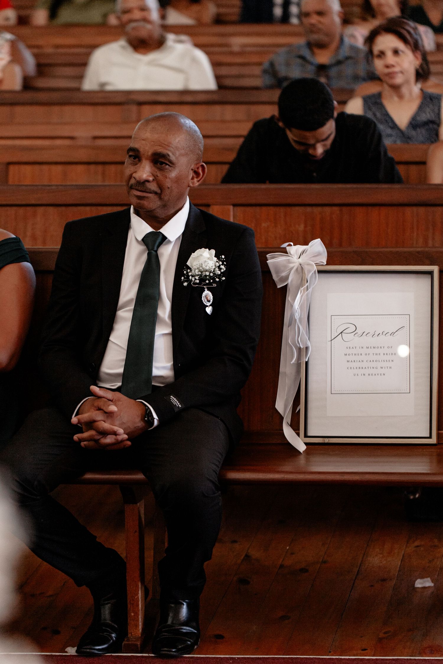 Guests sit in wooden church pews adorned with white bows and reserved signs during a formal ceremony.