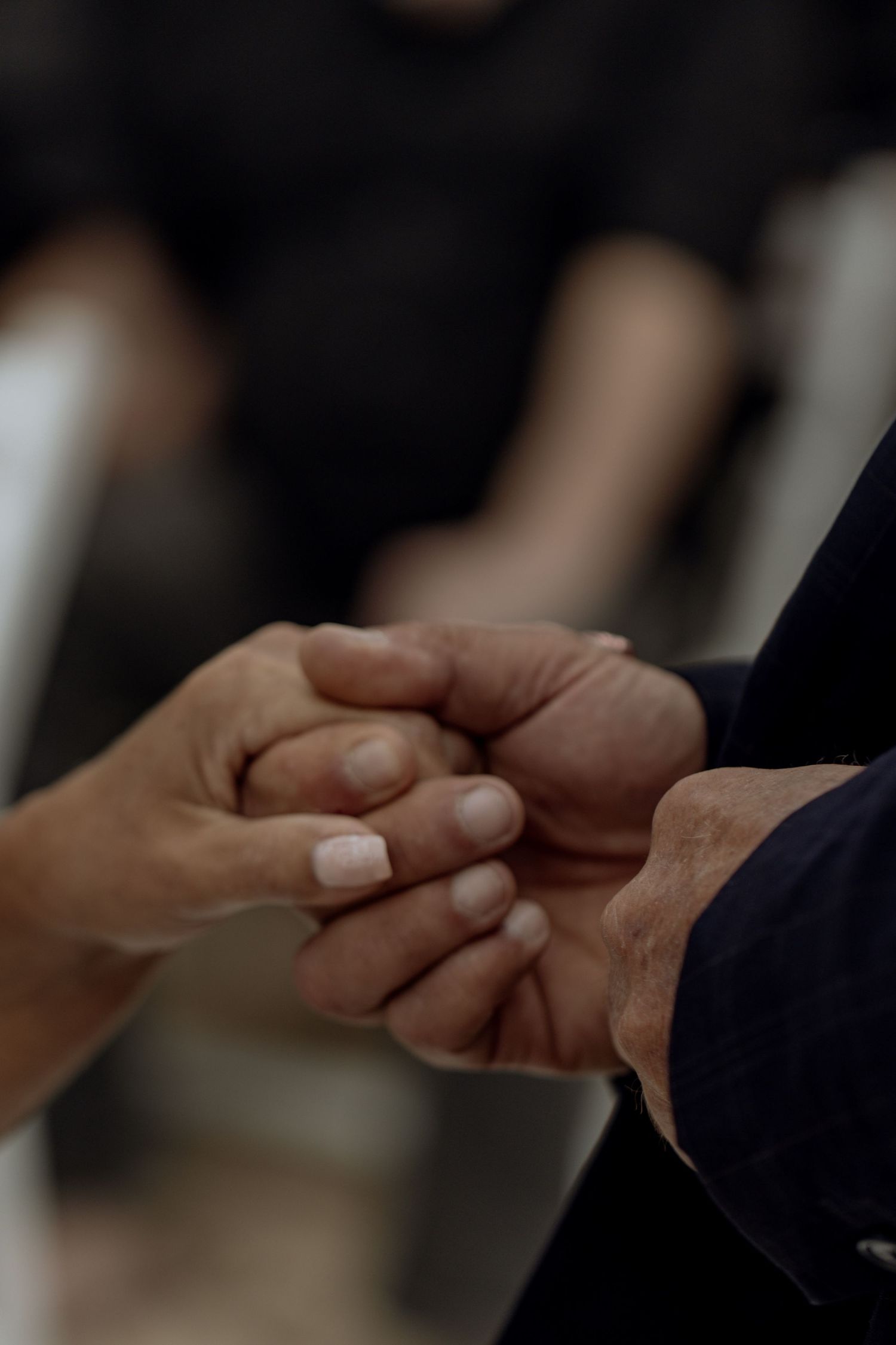 Two hands joining together in formal attire against a dark background, symbolizing business agreement or partnership.