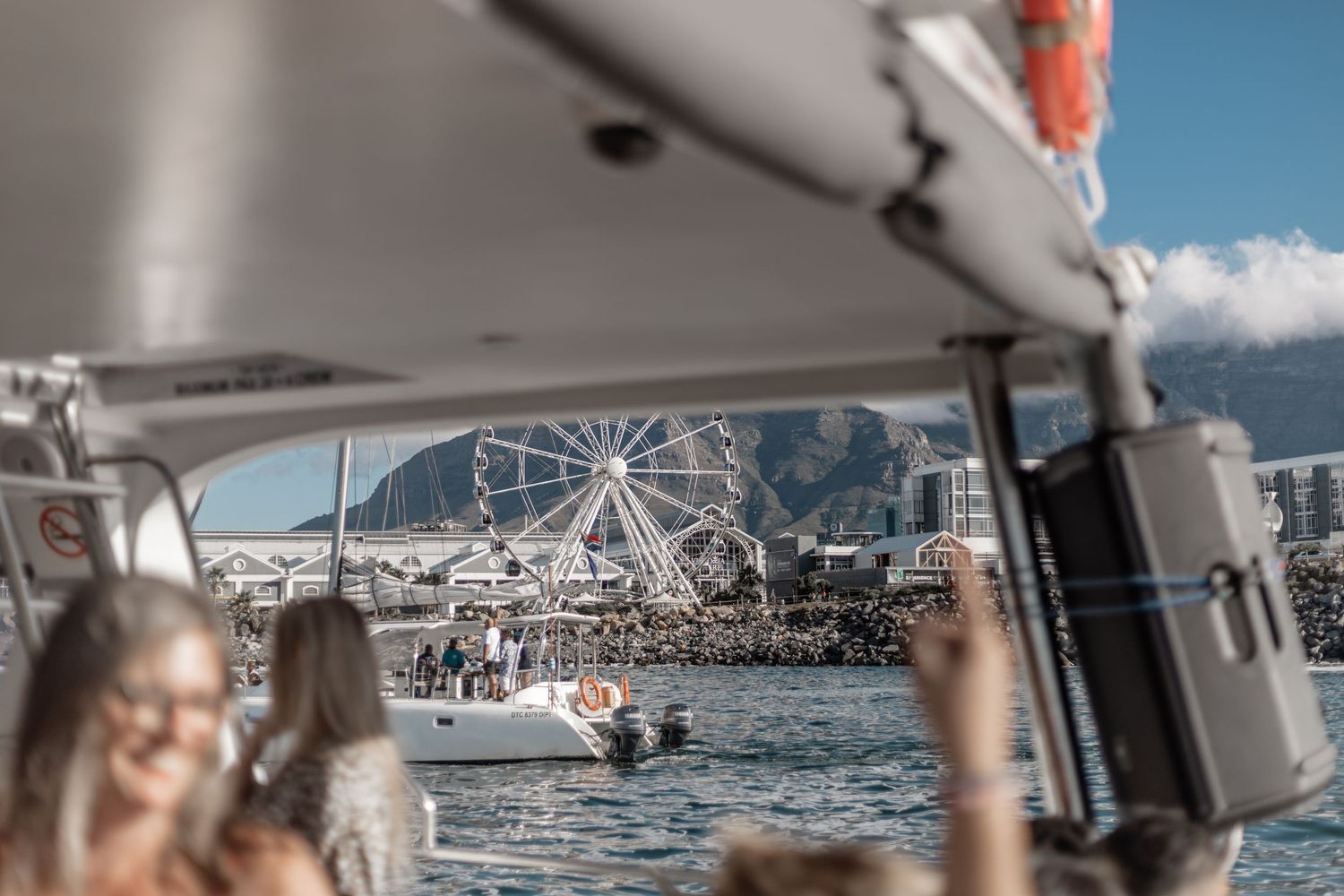 View of a ferris wheel and marina through a boat window frame on a sunny day at the waterfront.
