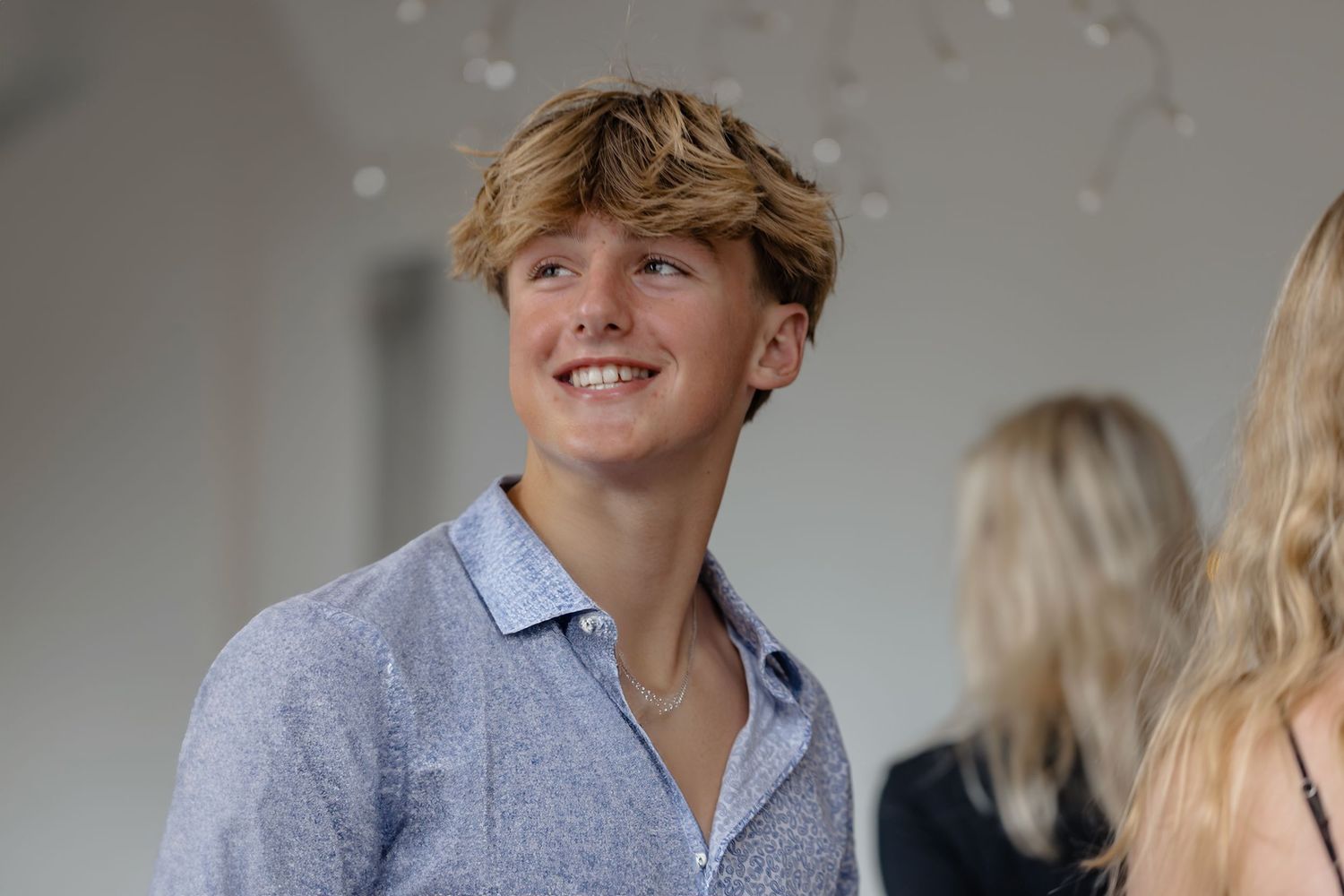 Smiling teenage boy with blonde hair wearing a light blue button-up shirt at a formal event.