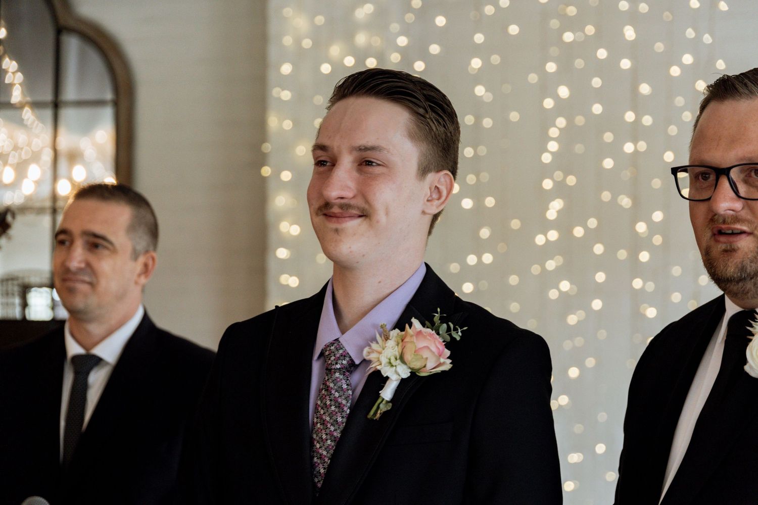 Wedding scene with fairy lights twinkling in background during indoor ceremony.