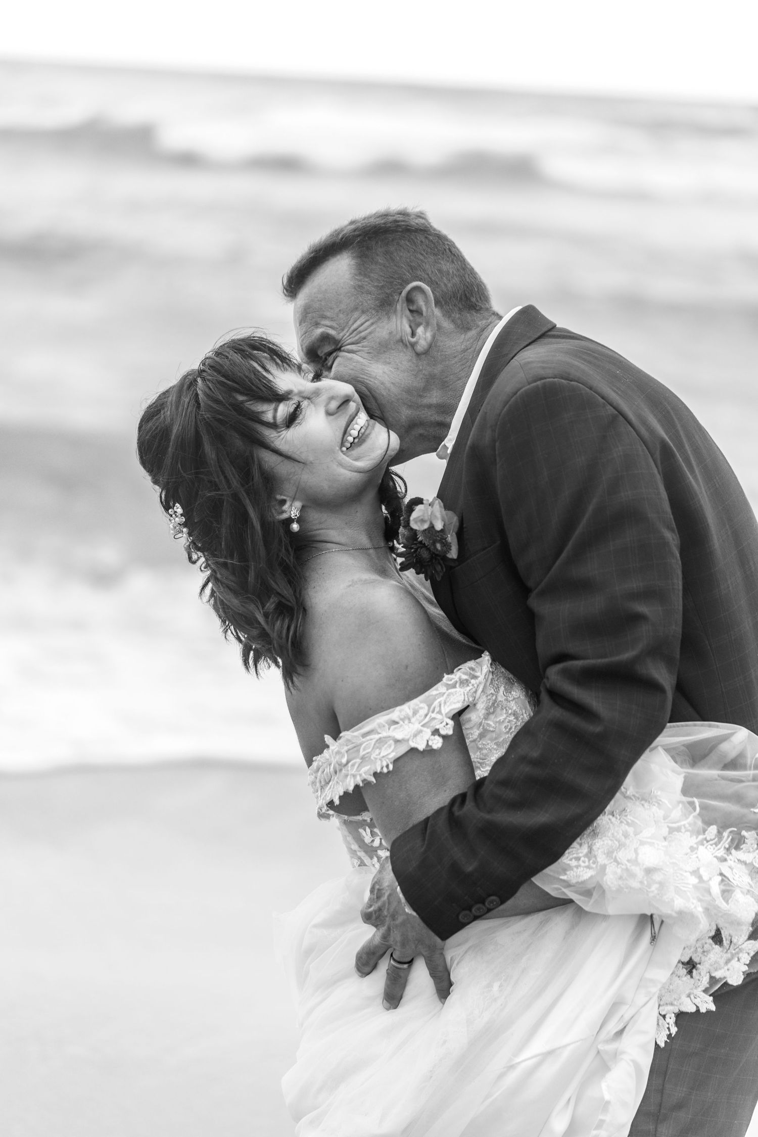 A romantic black and white beach wedding photo shows a happy couple sharing an intimate moment at sunset.