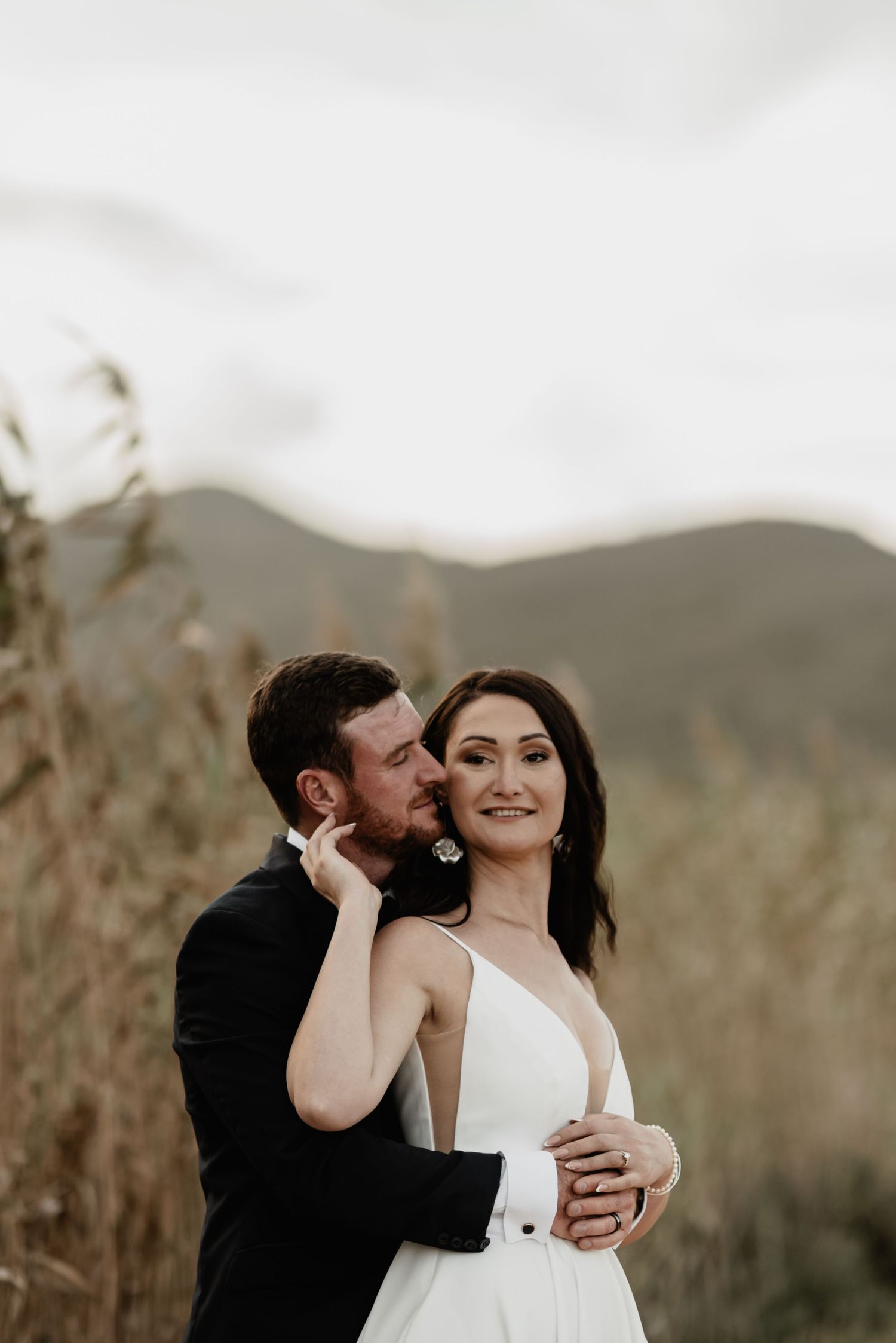 A couple shares an intimate moment in formal attire against a scenic mountain backdrop.