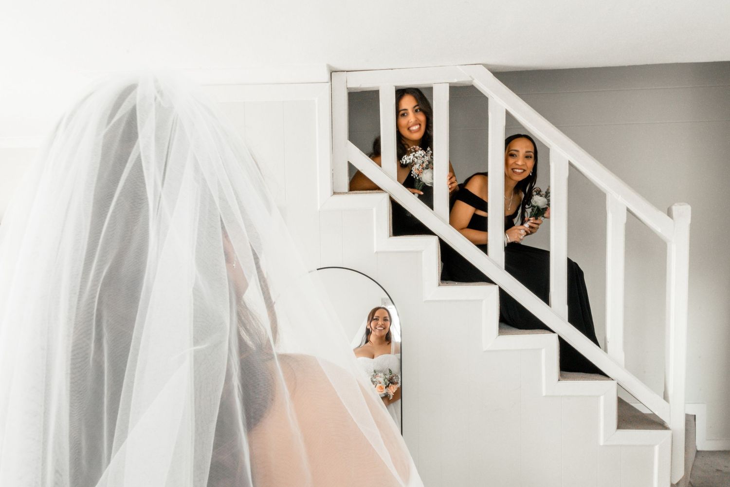 A bride in a flowing white veil descends a white staircase in an elegant indoor setting.
