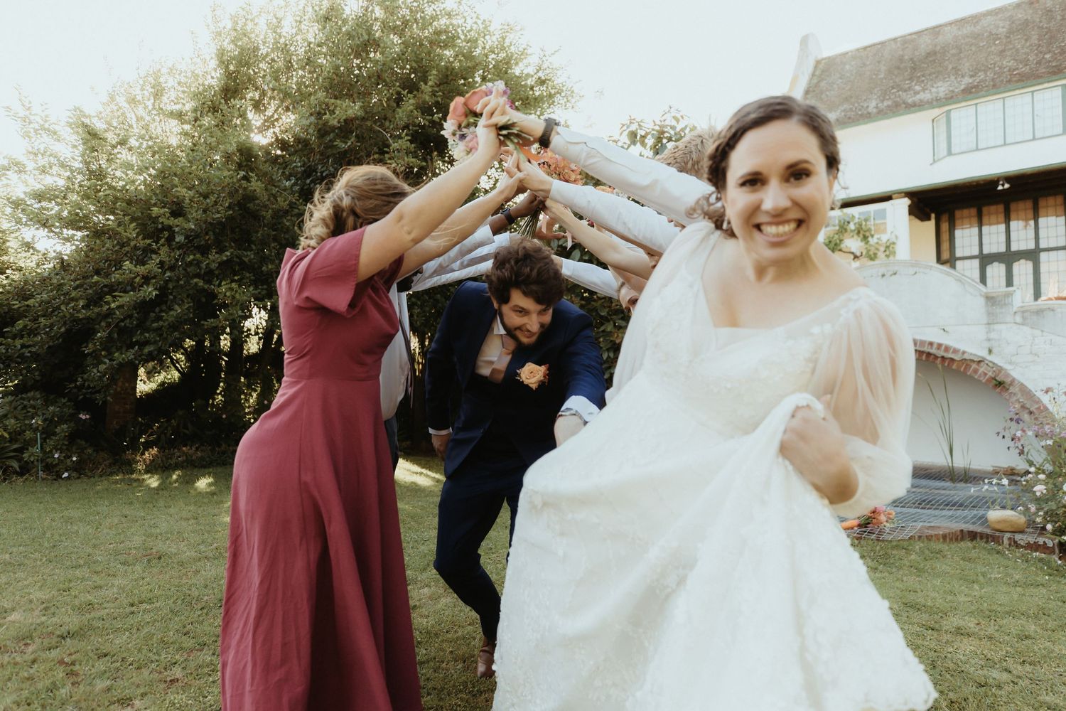 Wedding party celebrates on a lawn with people dancing and twirling in burgundy bridesmaid dresses and white gown.