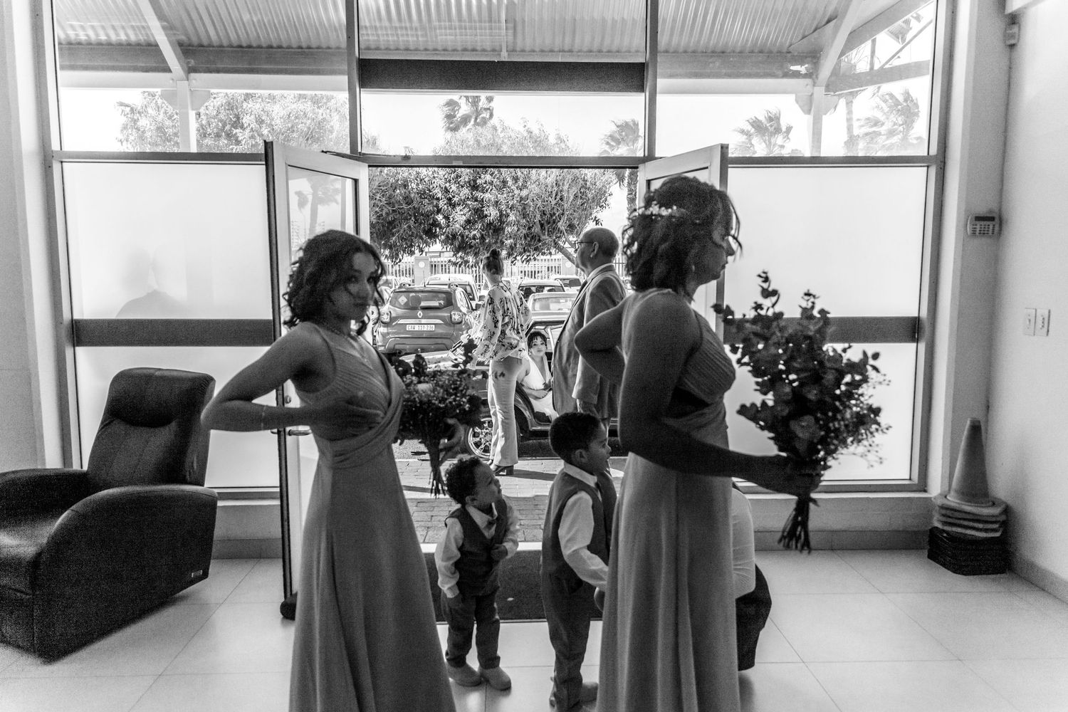 Patients waiting in hospital lobby with wheelchairs and medical staff visible through glass doors and windows.