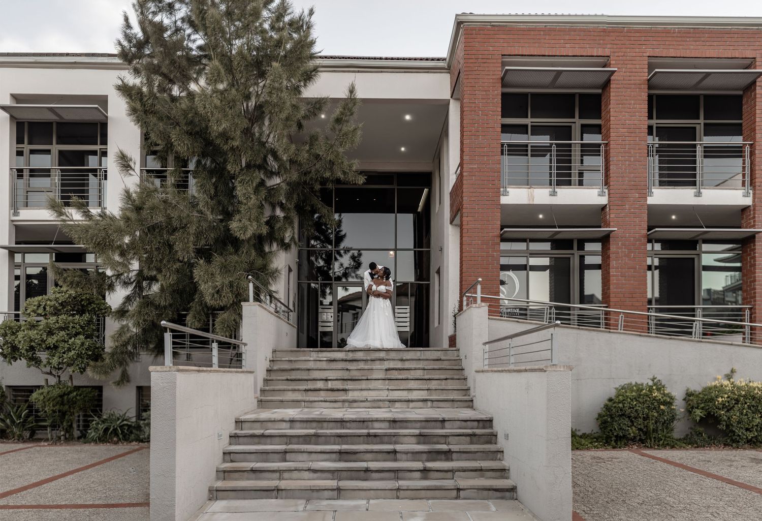 Panoramic view of a modern brick building entrance with concrete steps and glass windows at the entry.
