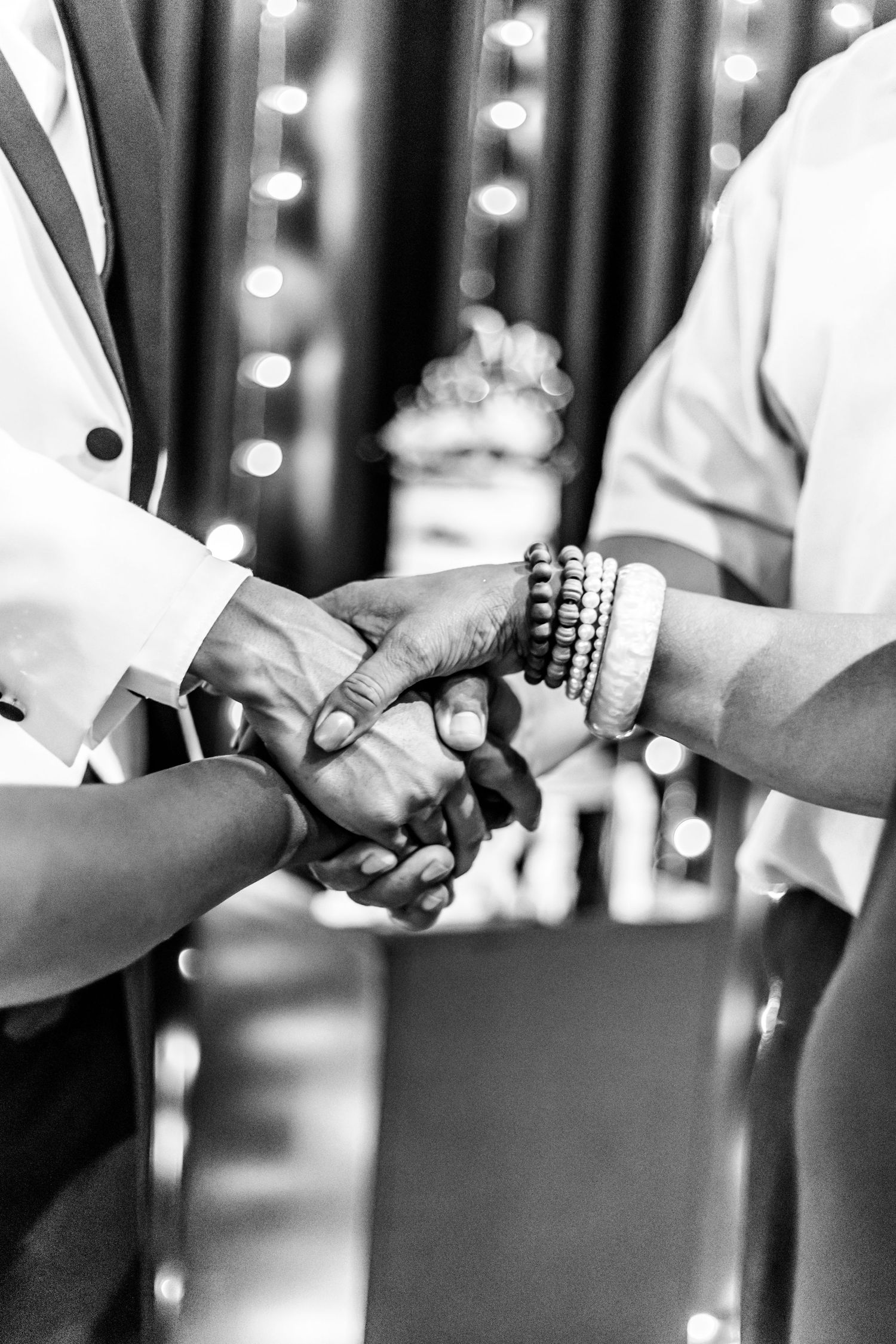 Black and white image of people exchanging wedding rings during a ceremony with bokeh lights in the background.