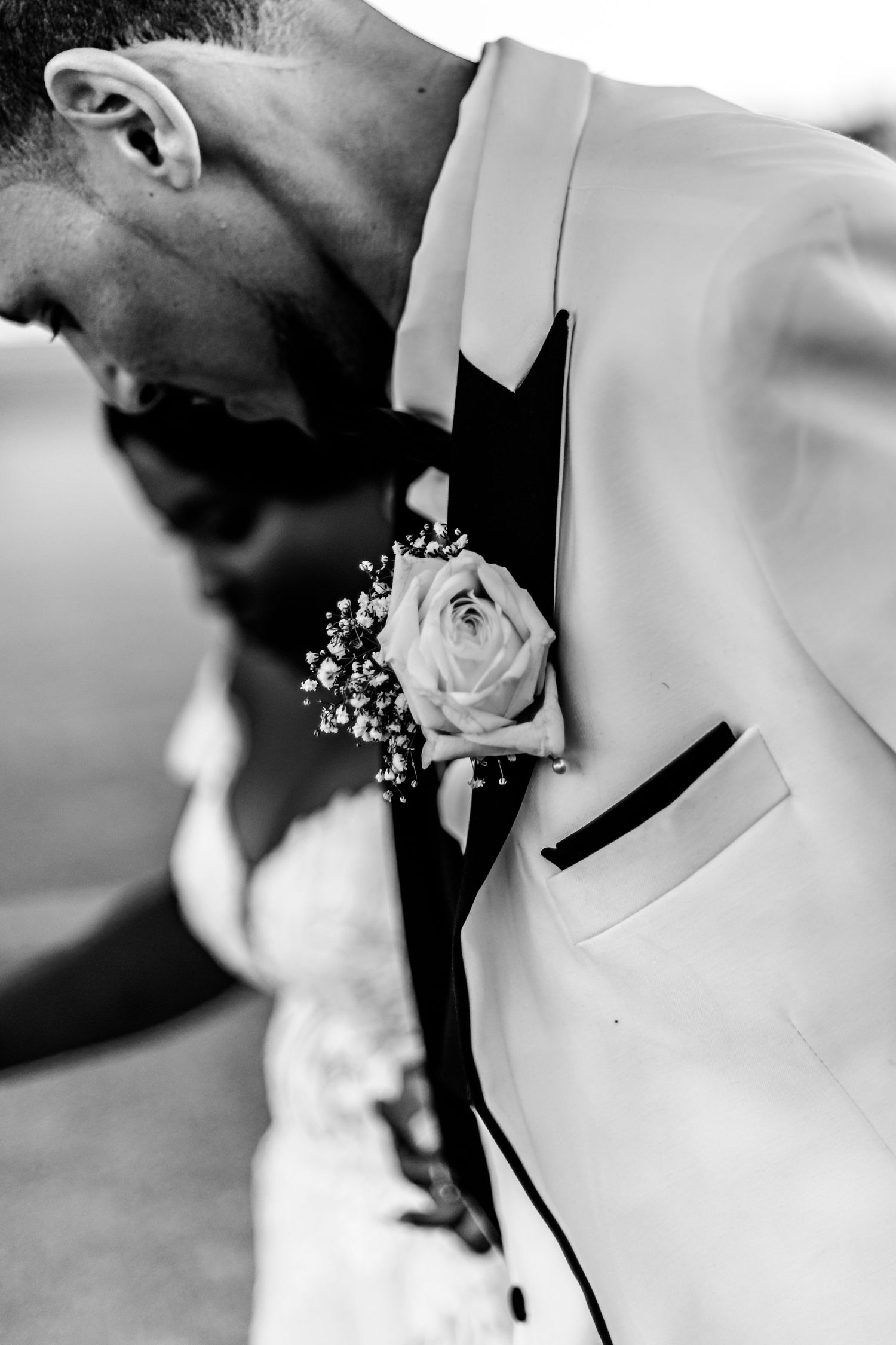 Close-up wedding details showing delicate floral bouquet and white dress fabric in black and white.