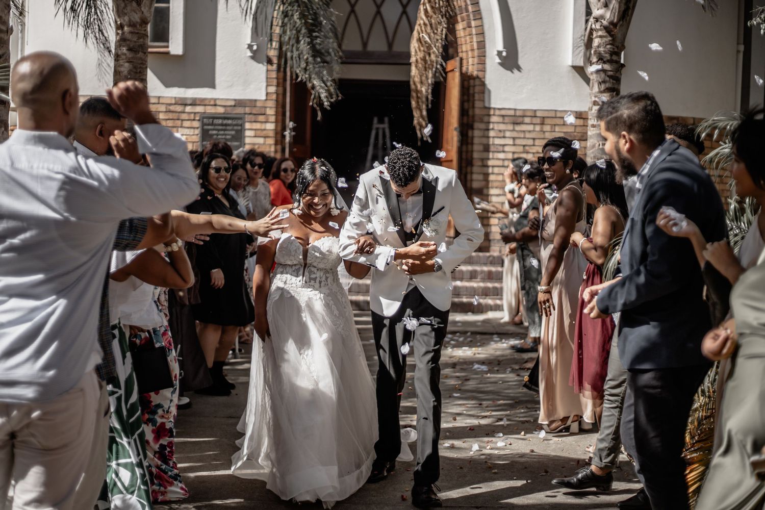 Wedding guests shower newlyweds with flower petals on church steps during outdoor ceremony celebration.