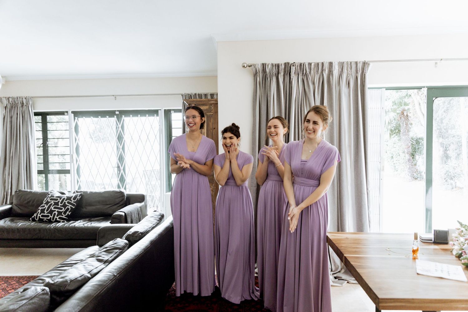 Row of bridesmaids dresses in soft lilac color hanging on display in a bright white room with natural lighting.