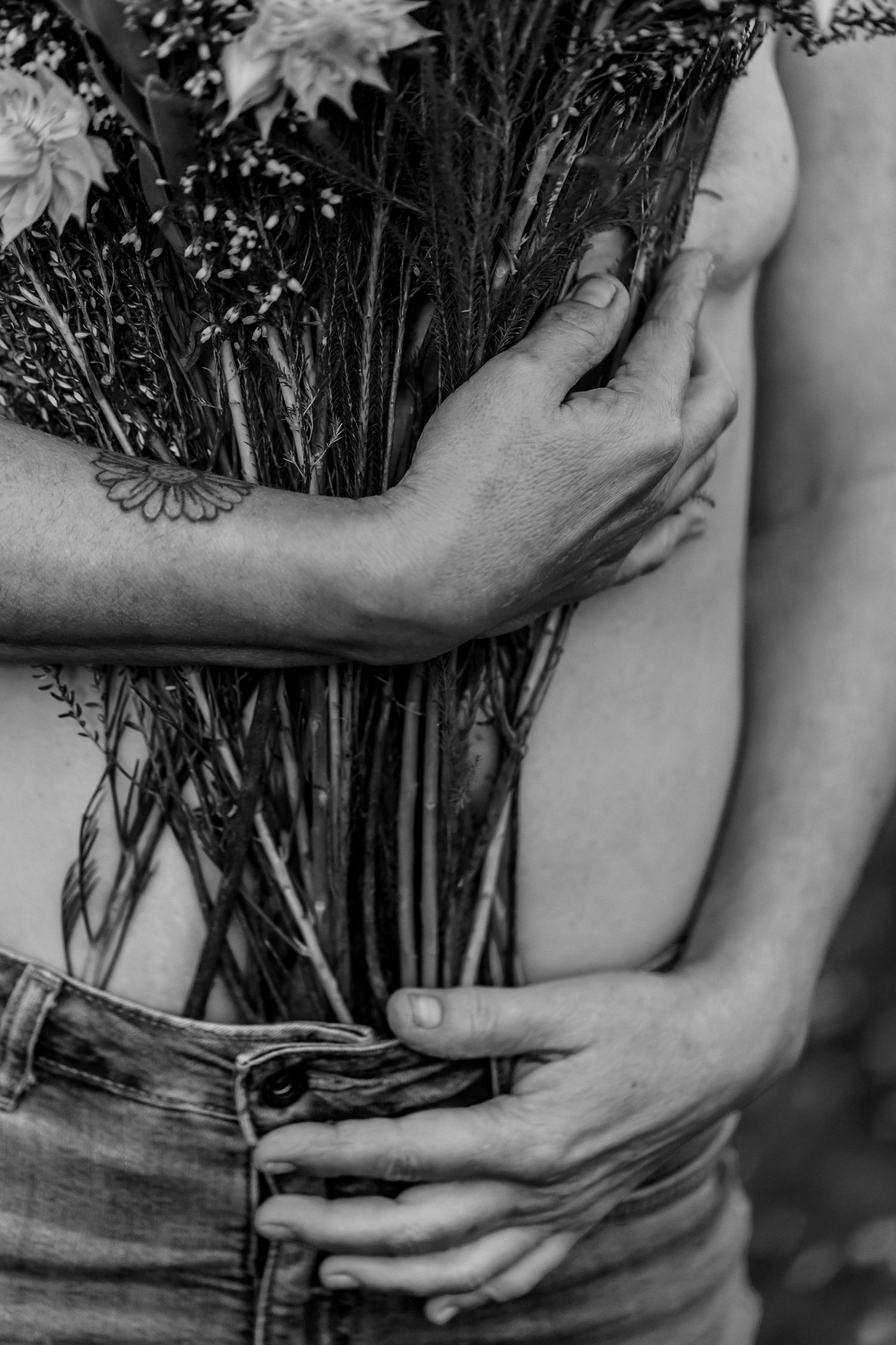 Black and white artistic photo of hands holding dried flowers against bare skin and denim jeans.