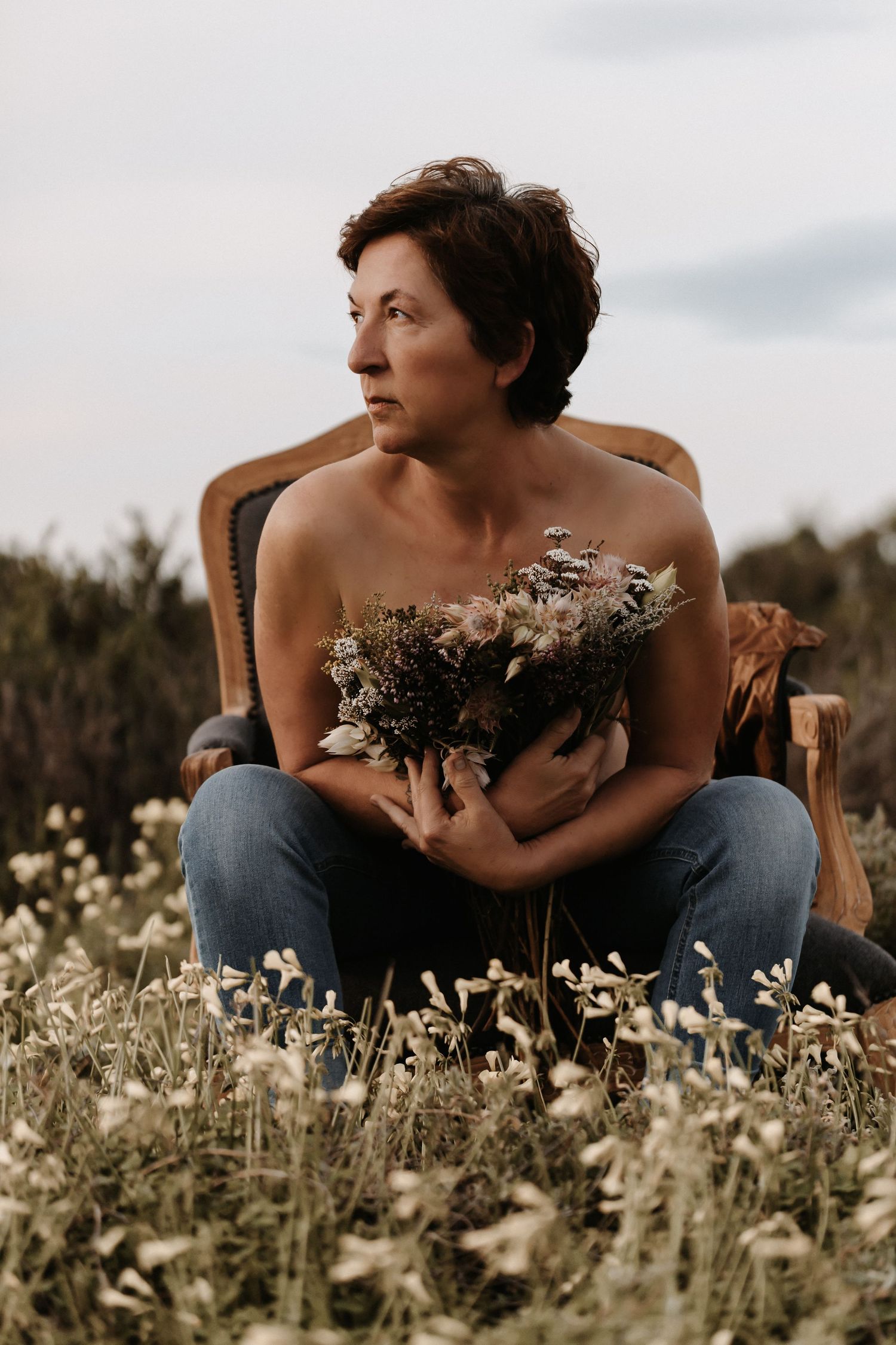 Artistic portrait in a wildflower meadow with someone sitting in a chair holding delicate dried flowers at sunset.