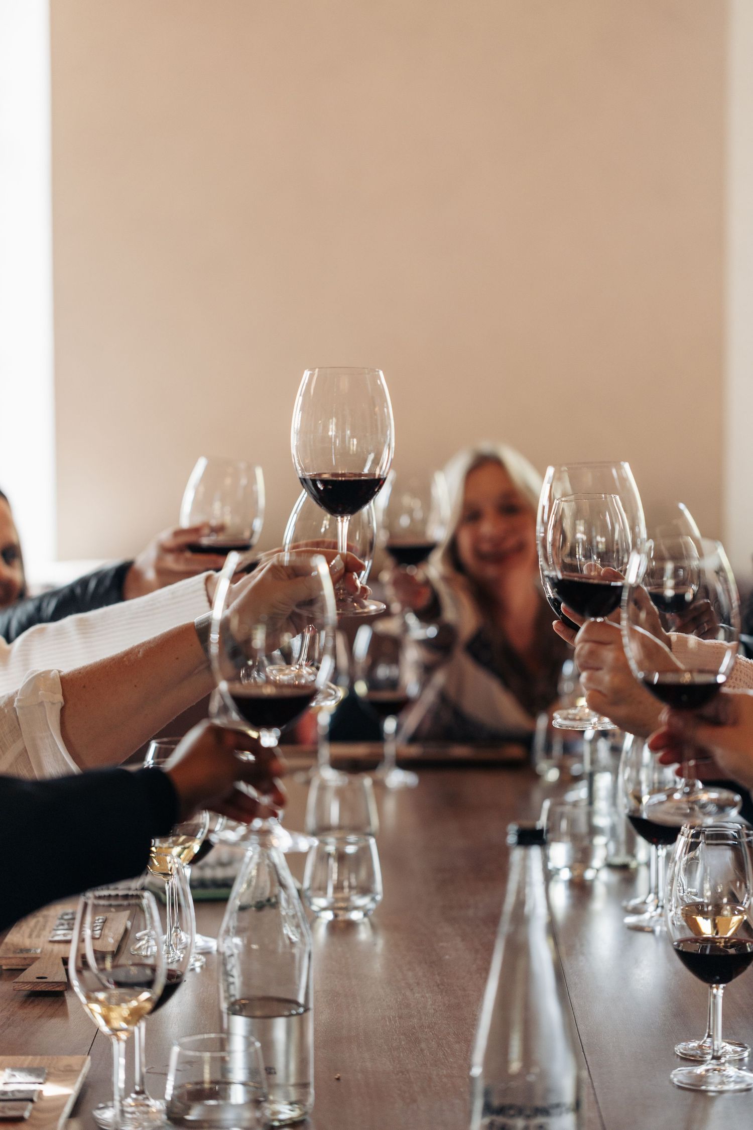 Group of people raising glasses of red wine in a toast at a restaurant table during a wine tasting event.