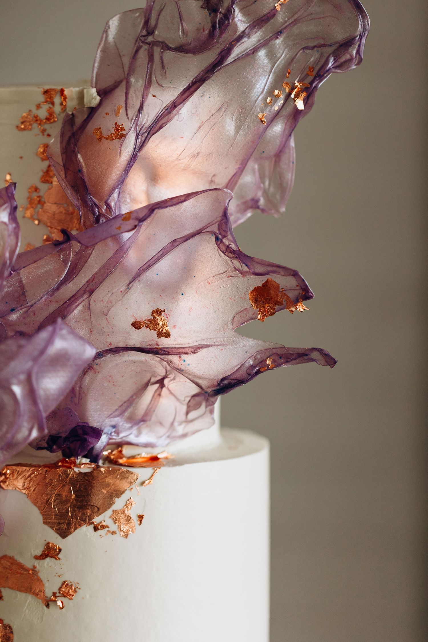 Elegant white wedding cake with purple sugar glass shards and copper gold leaf accents on a neutral background.
