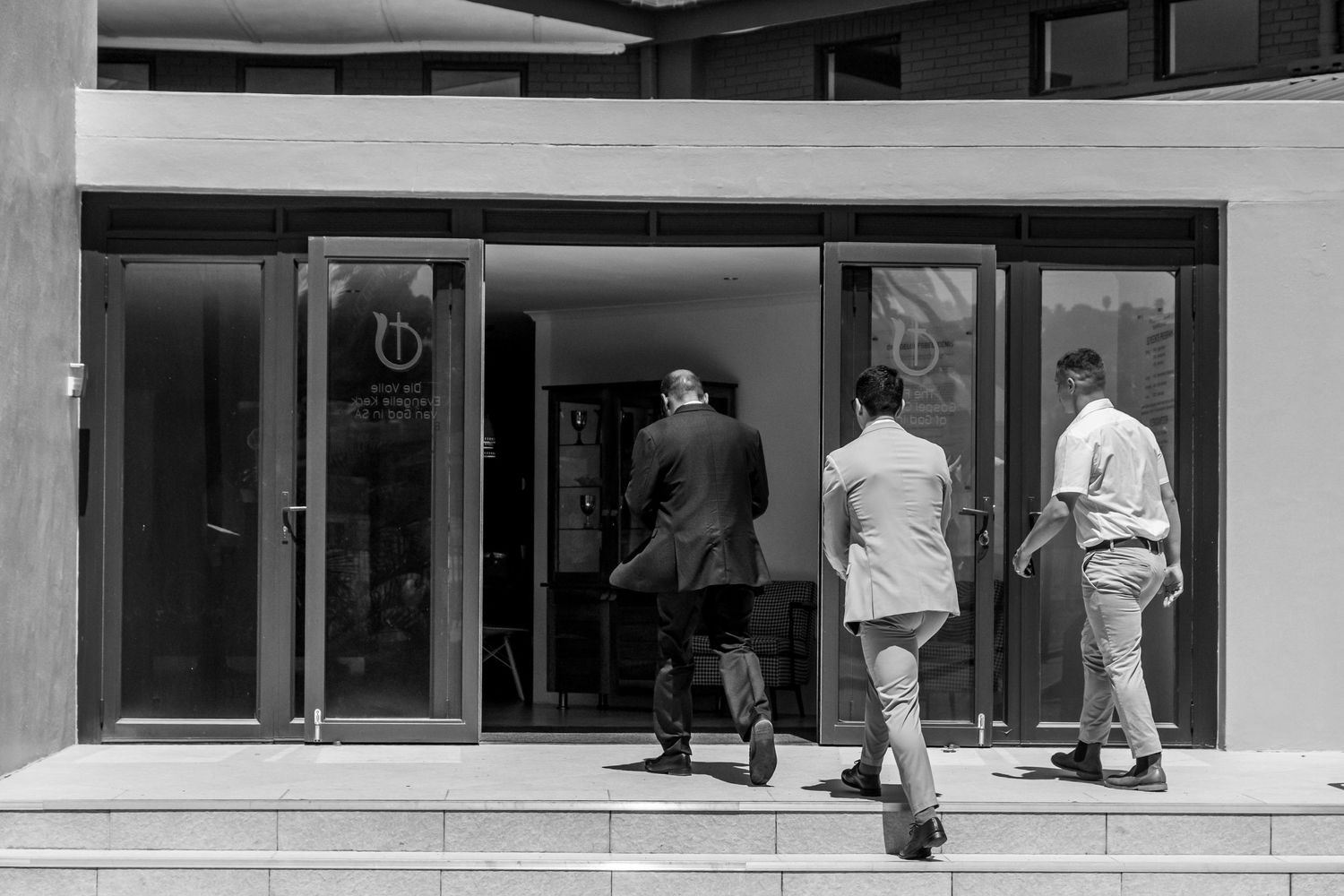 A black and white photograph shows a line of people waiting at windows in what appears to be an office building.