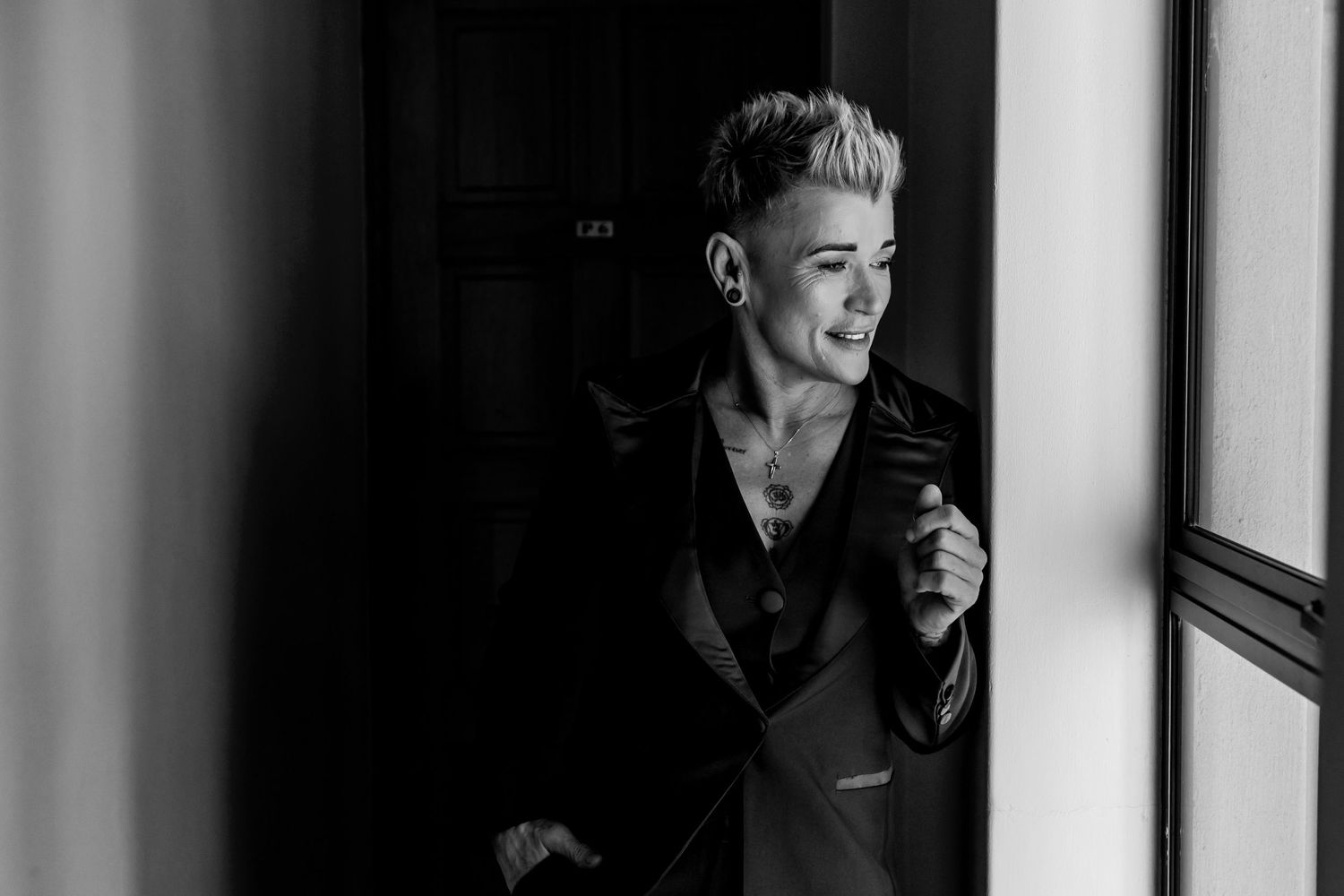 Black and white portrait photo of a person in dramatic lighting looking contemplative by a window.