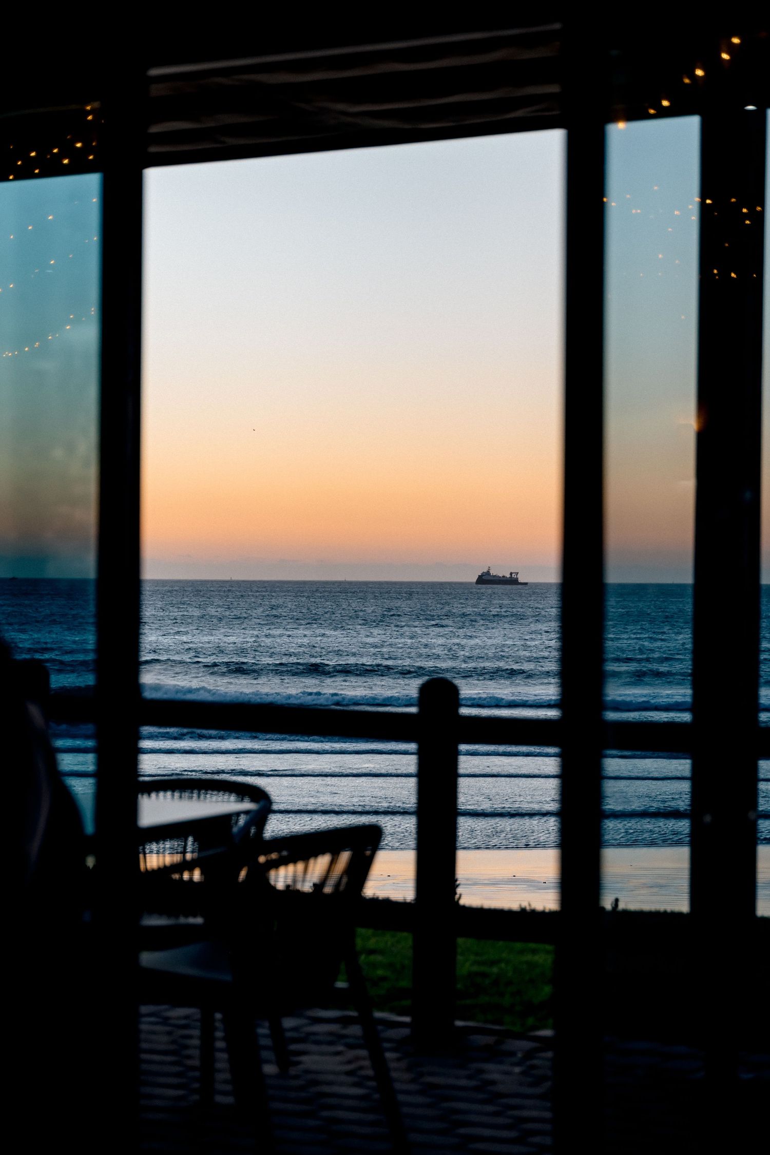 Ocean sunset view through a window frame with silhouetted furniture in the foreground.