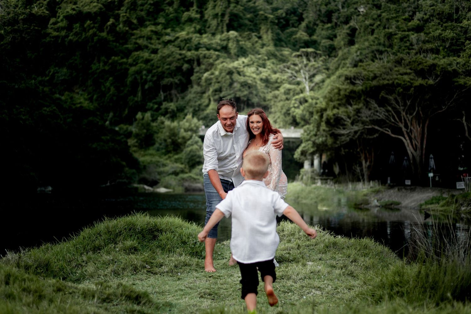 A couple walks hand in hand through lush green foliage during an outdoor engagement photography session.