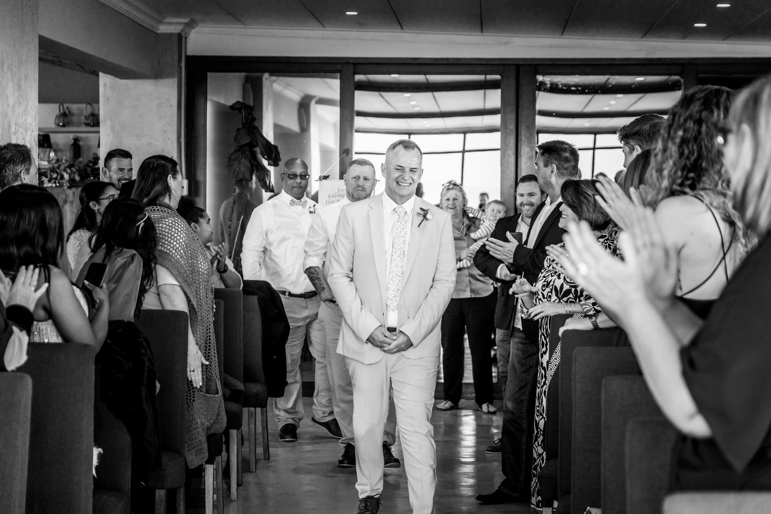 A wedding processional in a modern indoor venue with guests lining the aisle as someone walks down in black and white.