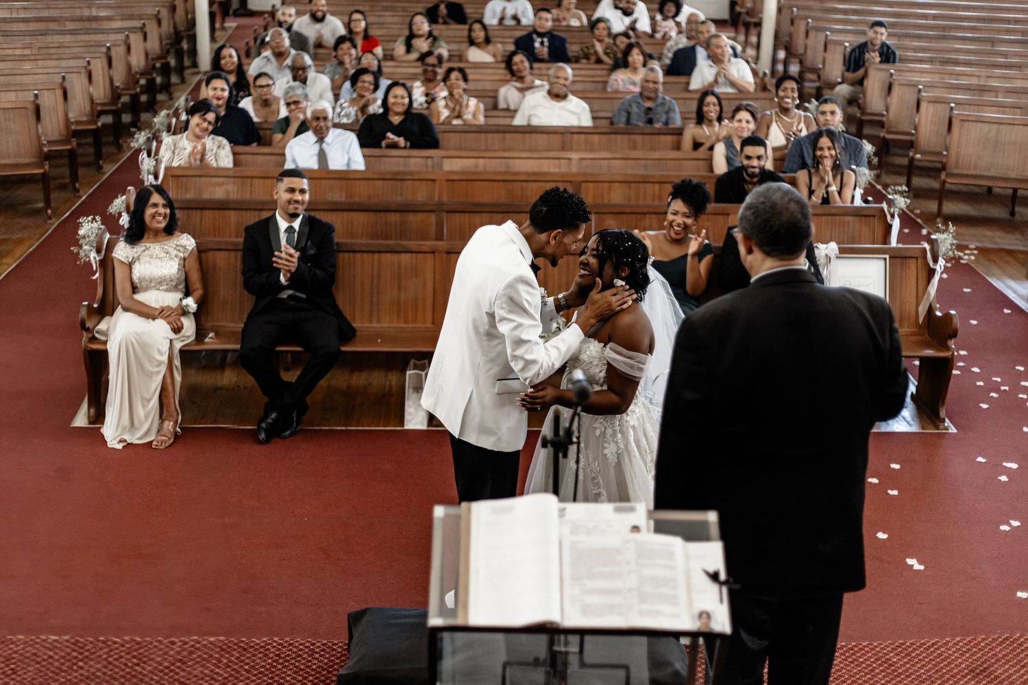 Two people sign marriage documents at a church altar while guests observe from wooden pews during a wedding ceremony.
