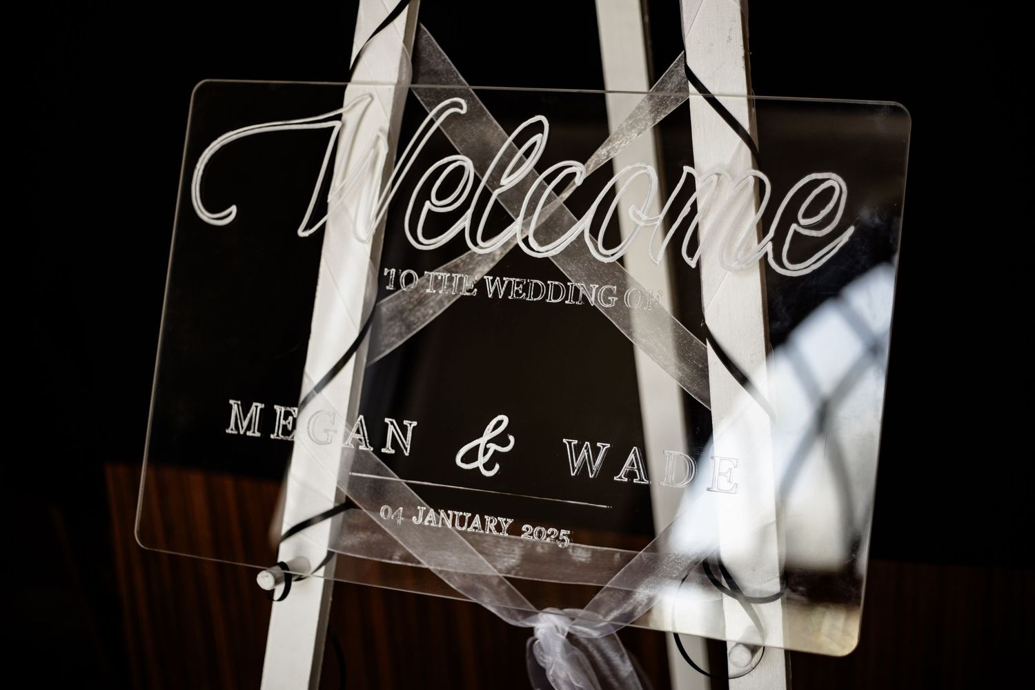 Clear acrylic wedding welcome sign with elegant script lettering and smoke wisps in soft lighting.