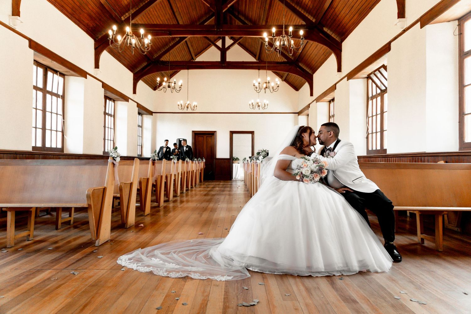 Bride and groom share a romantic pose in an elegant chapel with wooden pews and vaulted ceilings on their wedding day.