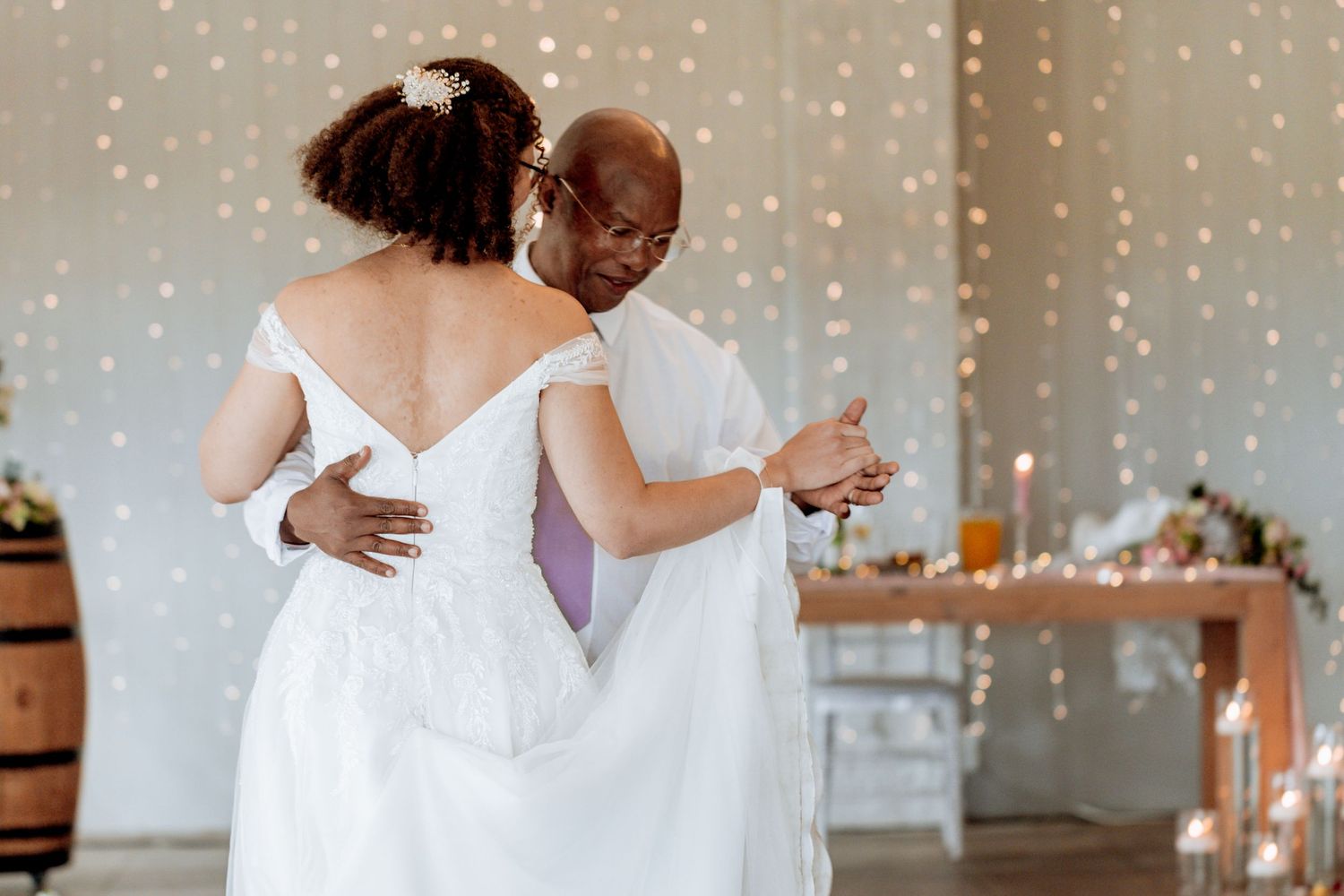 Wedding couple dancing together at elegant reception with twinkle lights and soft decorative lighting in background.