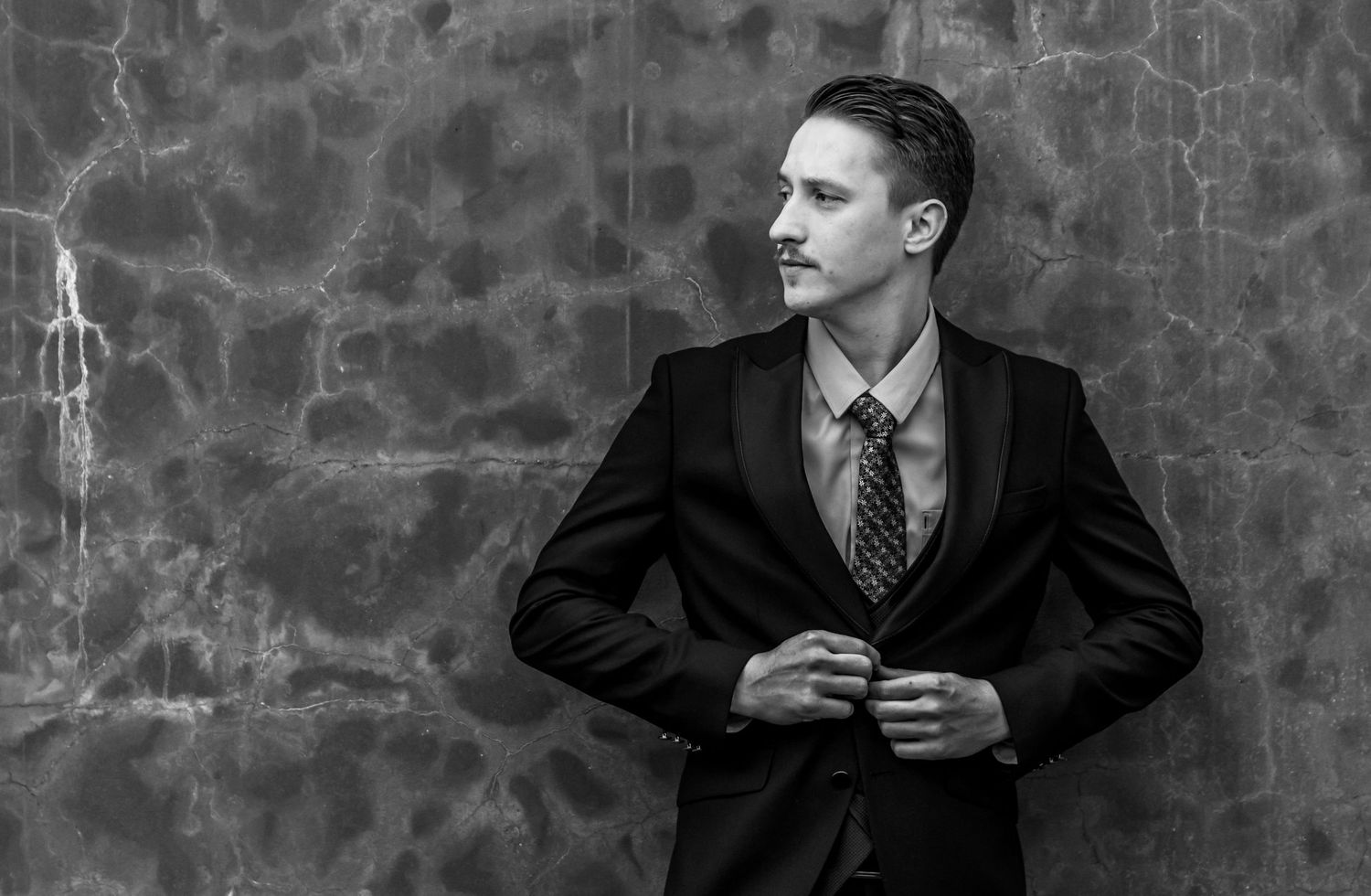 Four black and white images show someone in formal attire against a stone wall background.