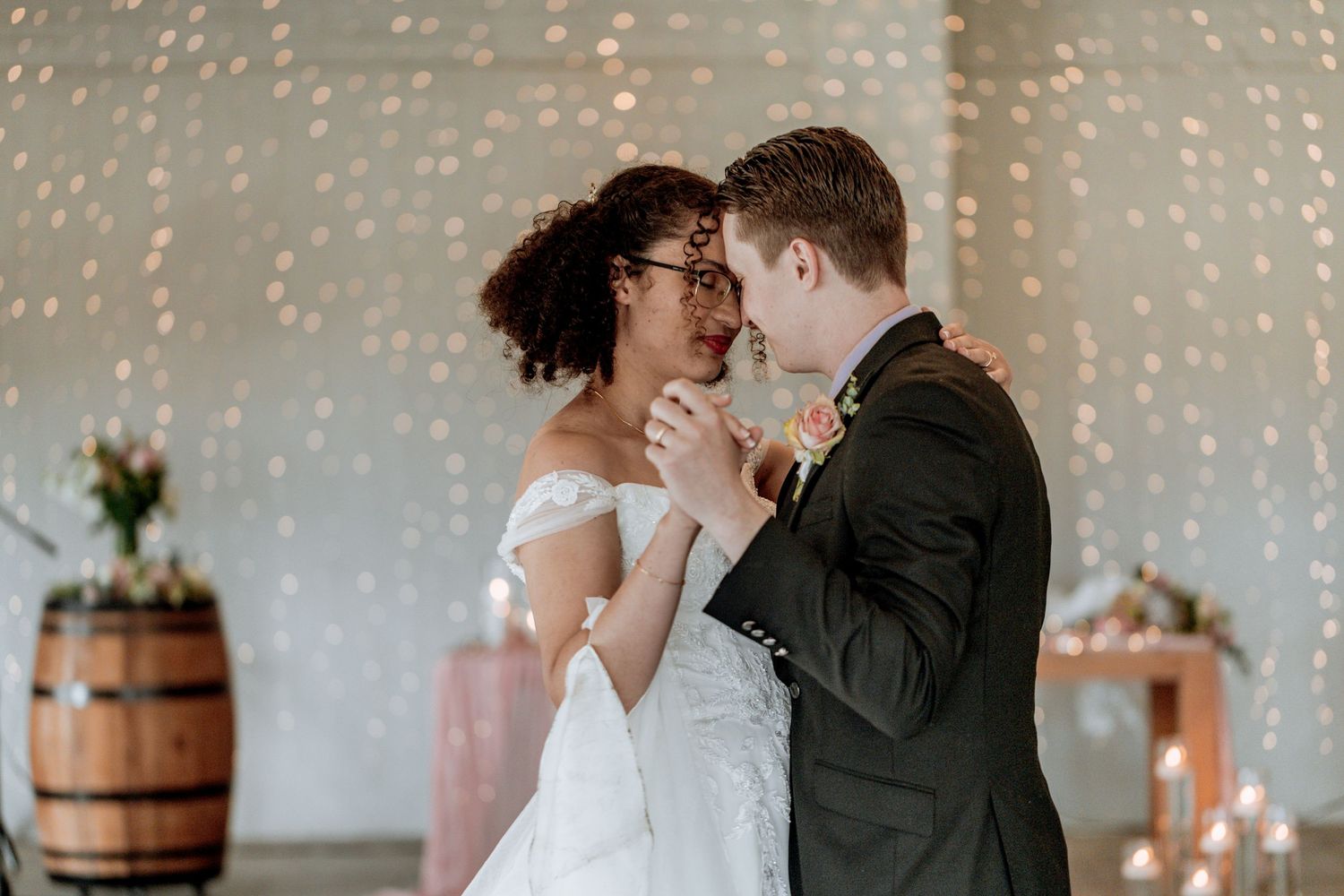 Couples share intimate moments during a romantic wedding celebration with twinkle lights and rustic wooden barrels.