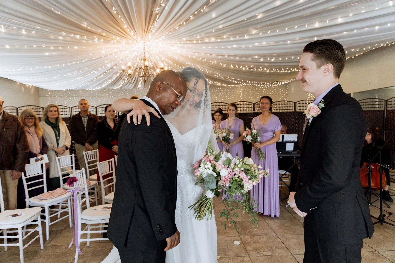 String lighting illuminates a white indoor reception venue with elegant drapery and formal event seating arrangements.
