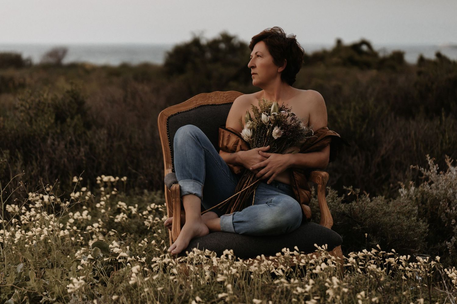 Couple sitting together in a blooming wildflower field during golden hour as sun sets behind rolling hills.