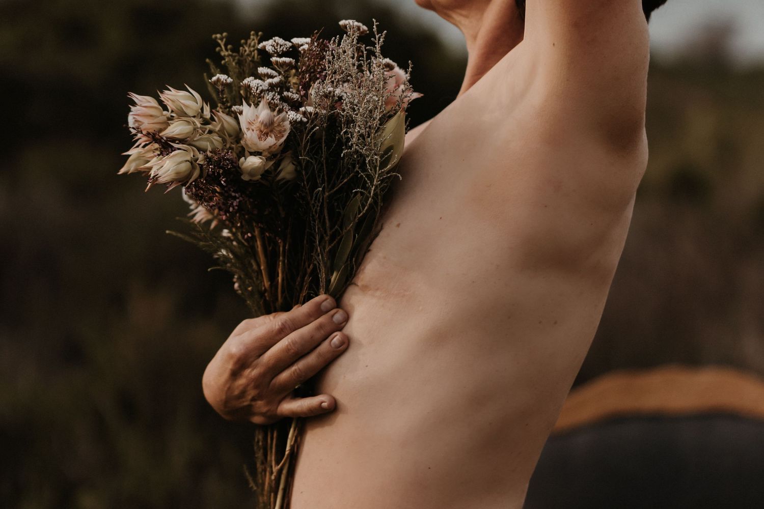 Hand holding a delicate bouquet of dried flowers in soft, muted tones against a dark background.