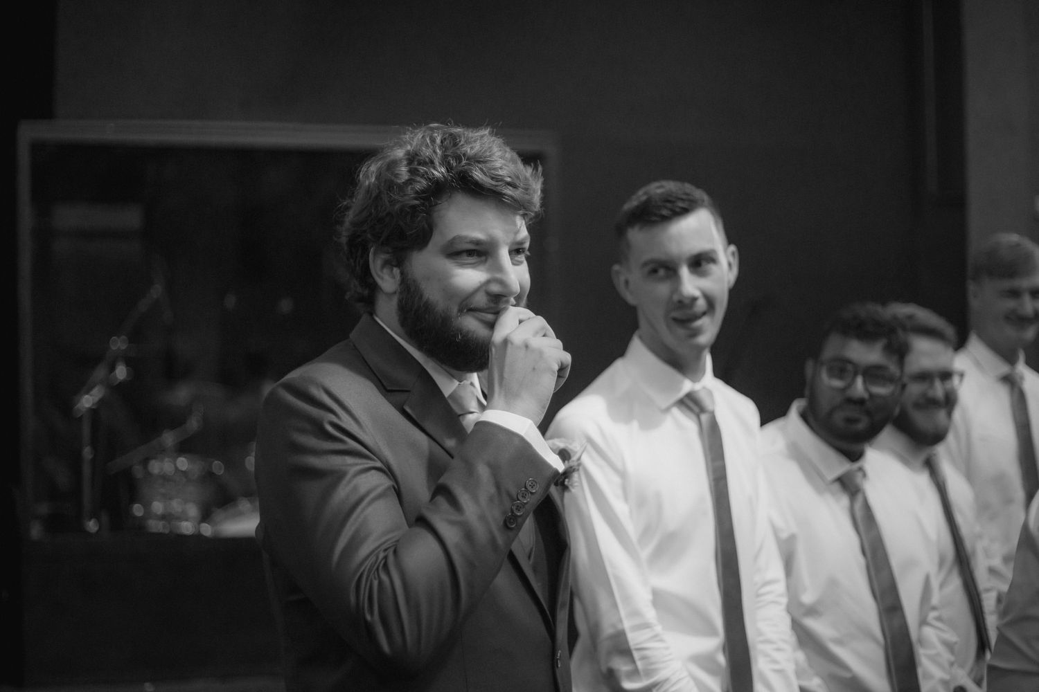 A black and white candid photo showing a bearded man in a suit laughing while standing with others at an event.