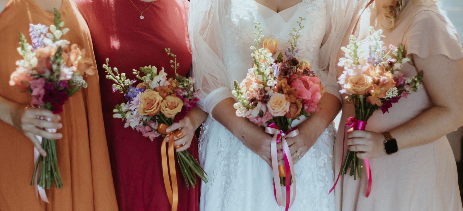 Wedding bouquets in shades of pink, burgundy and white with roses and mixed flowers held by hands in formal attire.