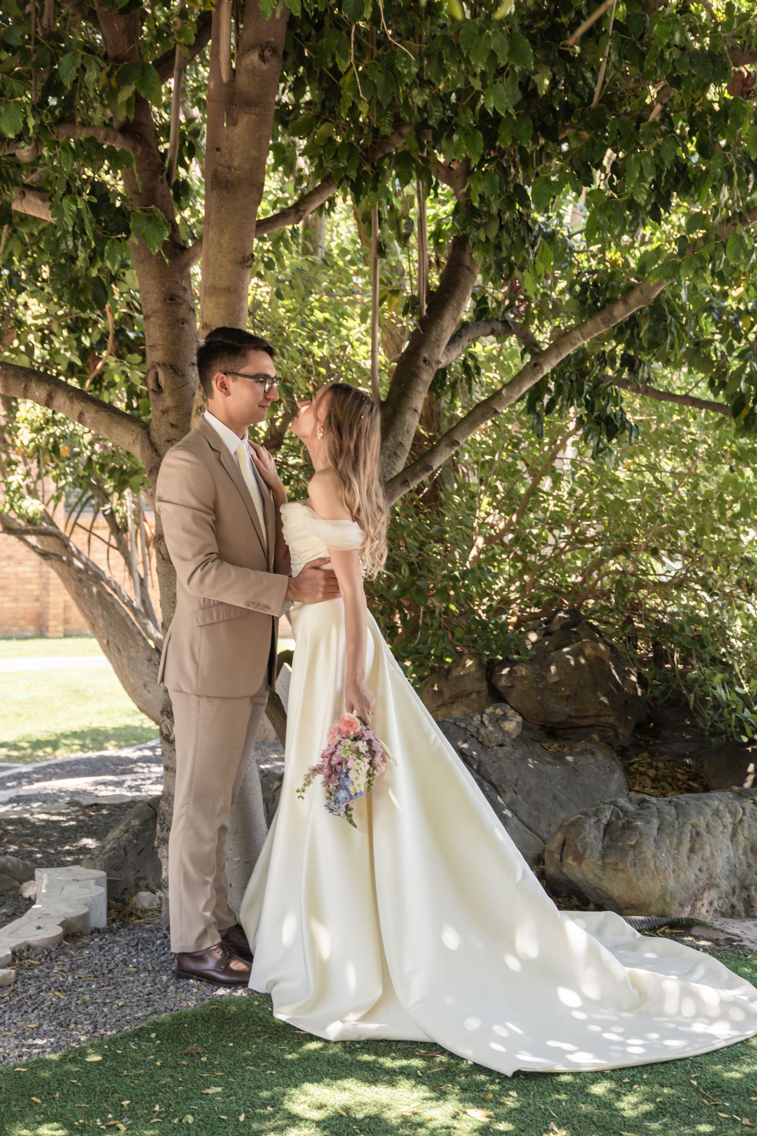 A couple shares a romantic moment under a leafy tree canopy during their outdoor wedding ceremony.