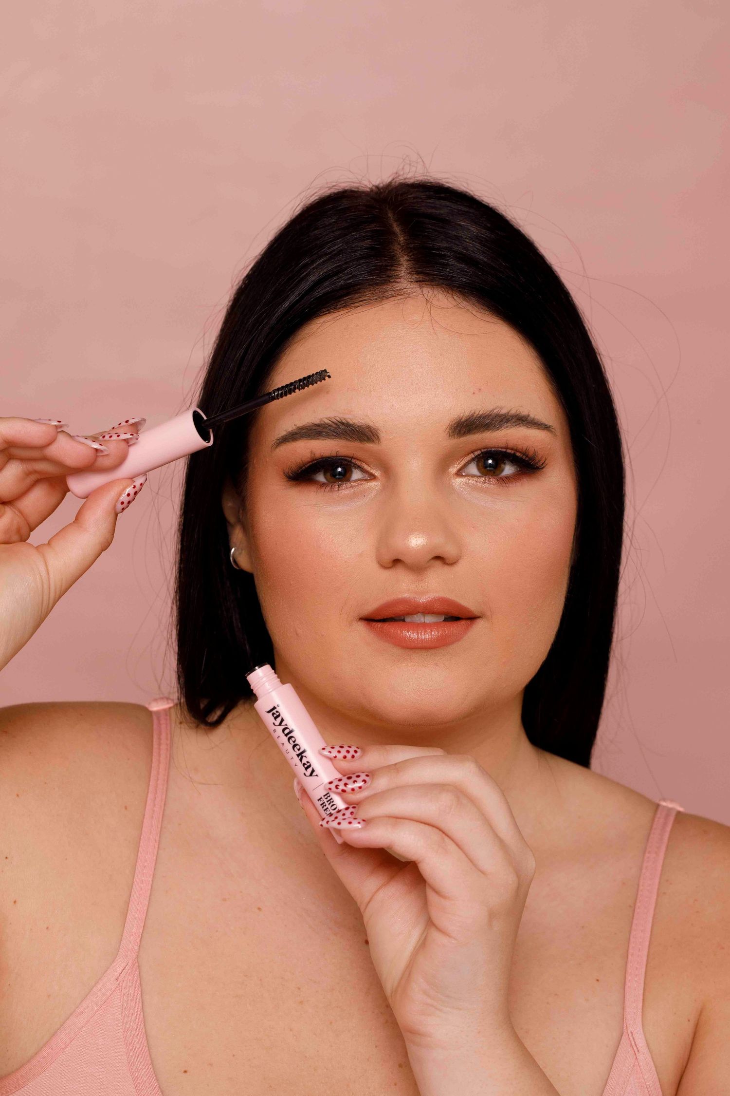 Beauty portrait with pink straps against rosy background showing makeup application with beauty tools.